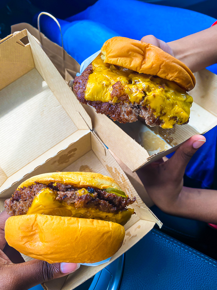 holding two OG burgers from Trill Burgers HTX.