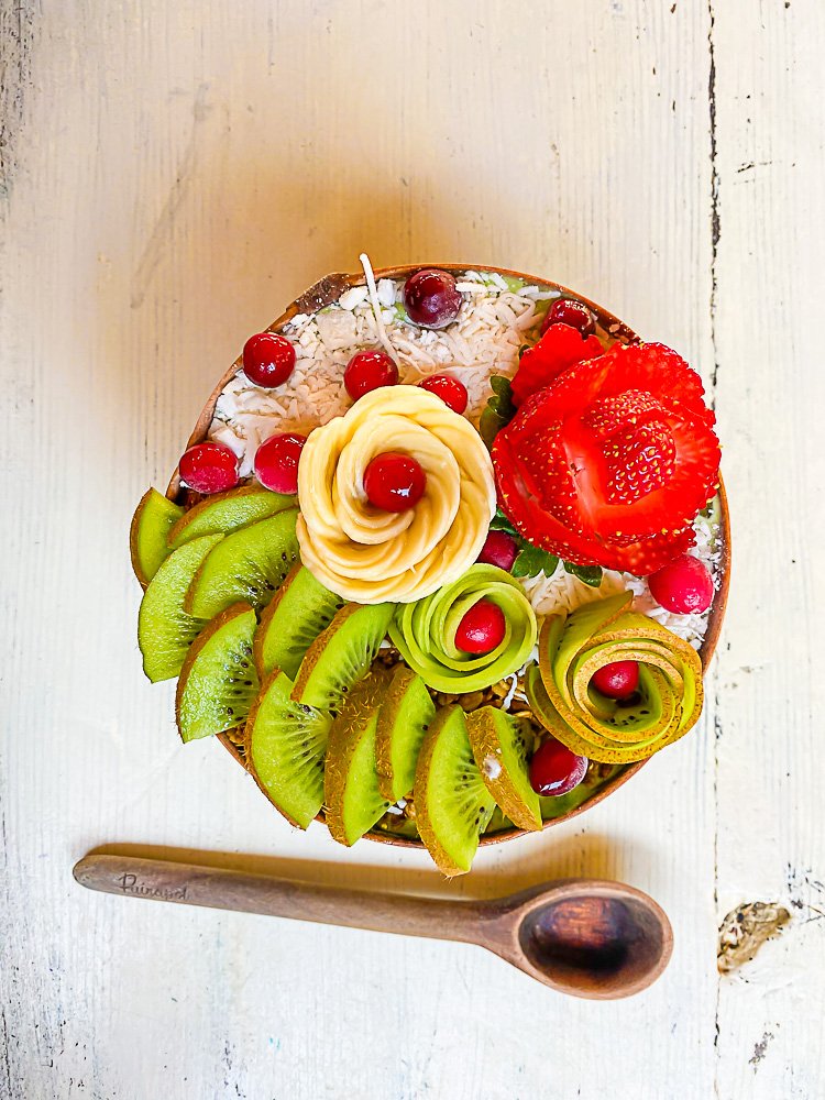 Grin smoothie bowl from adorned with fresh kiwi, banana slices, and berries arranged into flower shapes