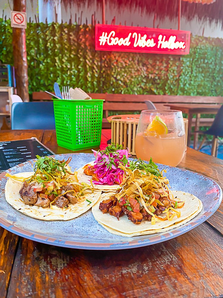 plate of three tacos on table top with neon sign in background reading "#Good Vibes Holbox"