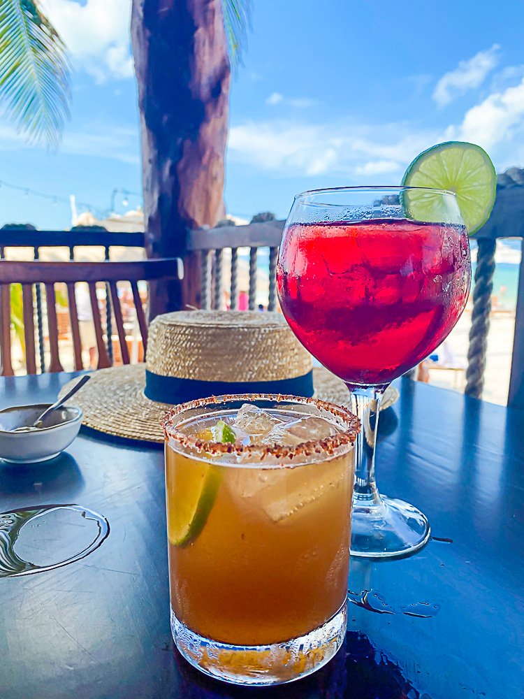 two cocktails on table in front of straw hat