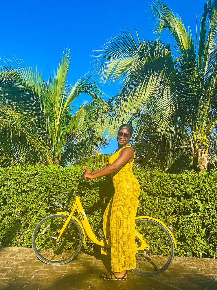 Jazzmine on yellow bike wearing a yellow crochet jumpsuit on a sunny day.