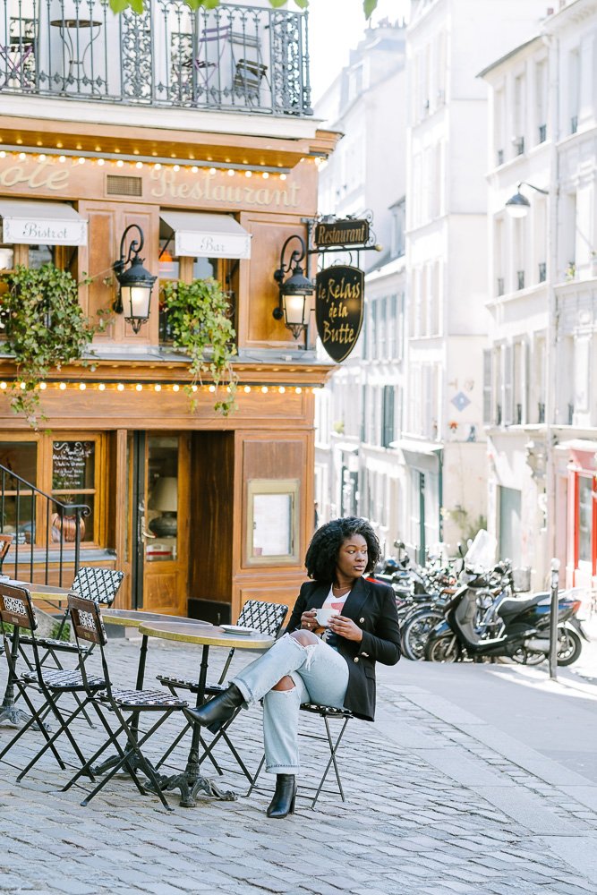 Jazzmine sitting at cafe table holding cup of coffee.