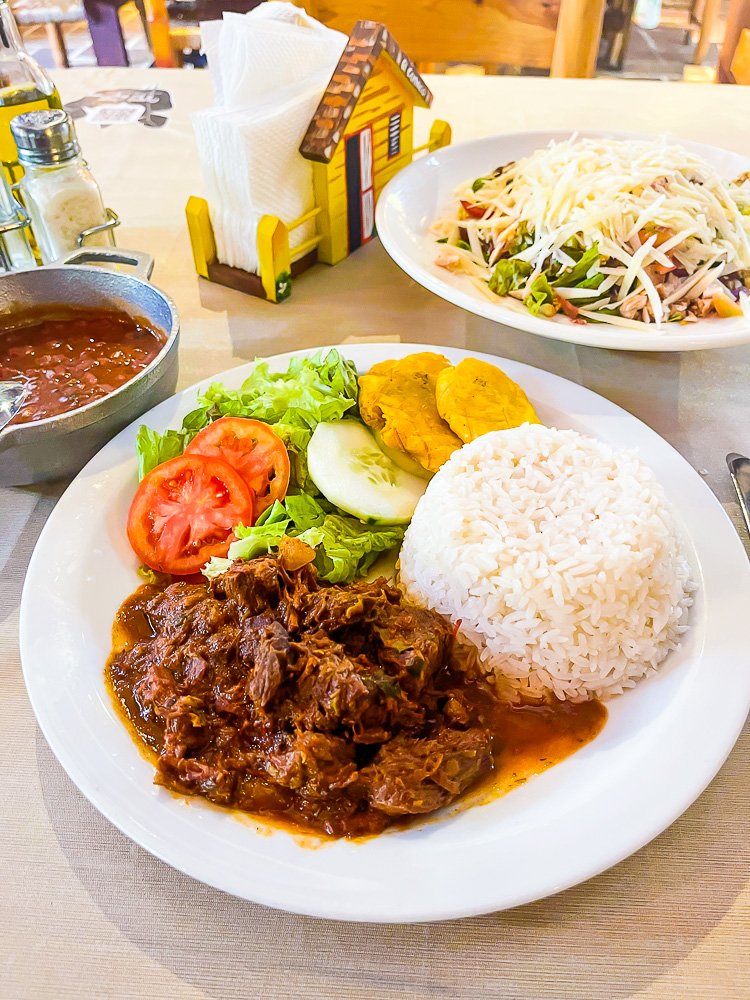 authentic dominican plate of stewed beef, rice, tostones, and vegetables.