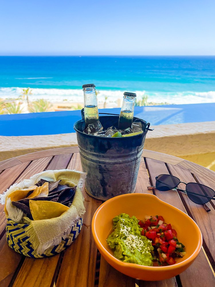 bucket of coronitas, sunglasses, and chips with guacamole and pico de gallo on table overlooking private pool and Sea of Cortez.