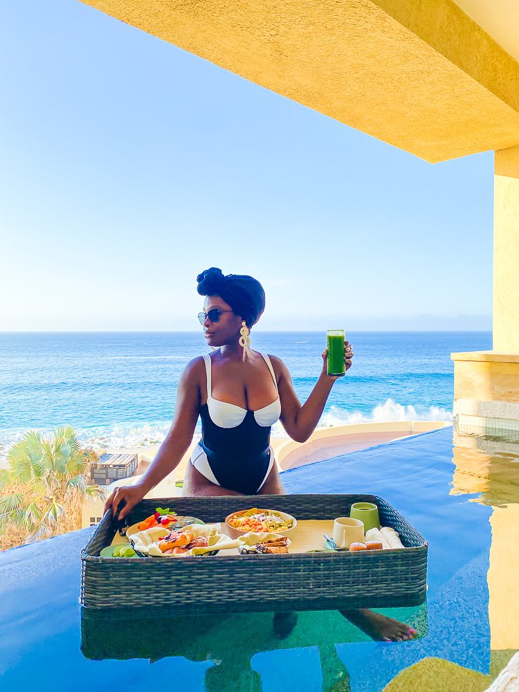 Jazzmine sitting in private terrace pool holding tall glass of green juice with floating Mexican breakfast.