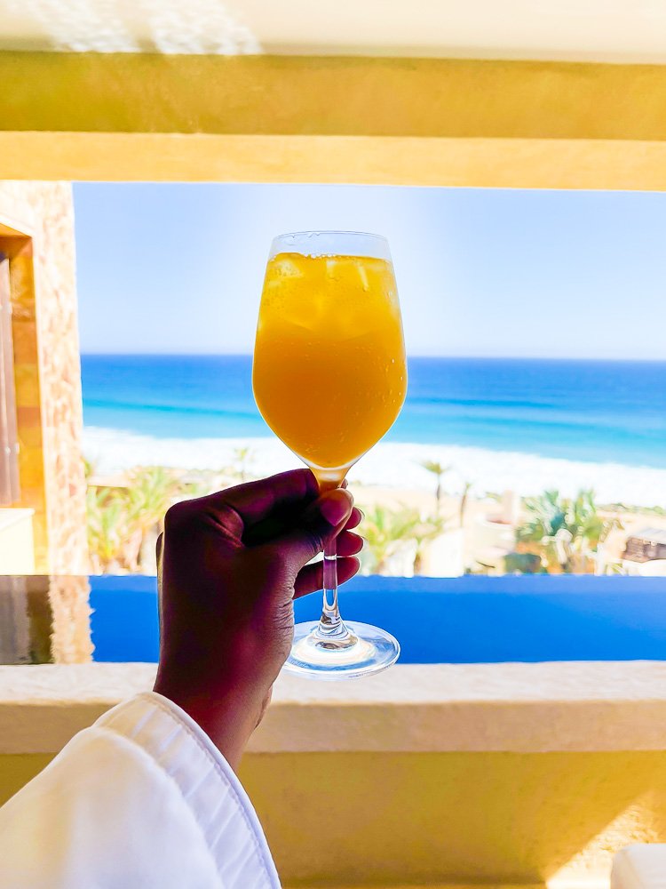 holding up mimosa with ocean in background.