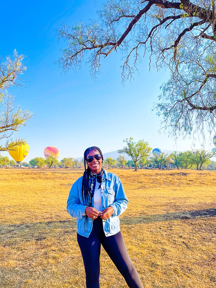 Jazzmine standing in a field near Teotihuacan with hot air balloons landing in the background.