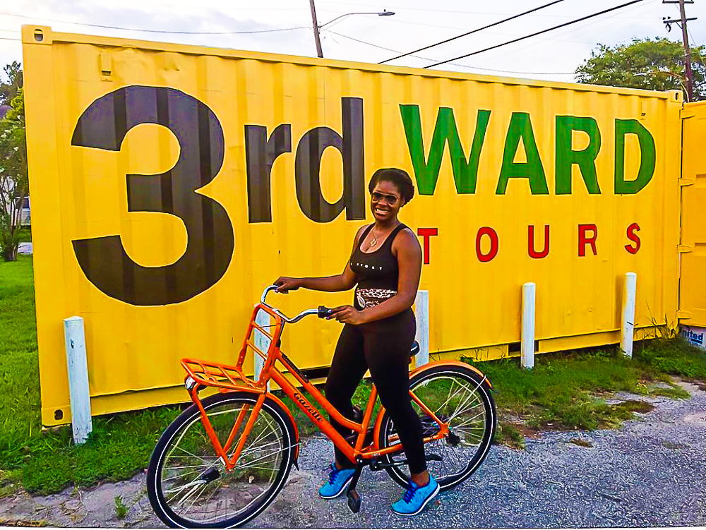 Jazzmine on orange bike in front of yellow sign that reads 3rd Ward Tours.