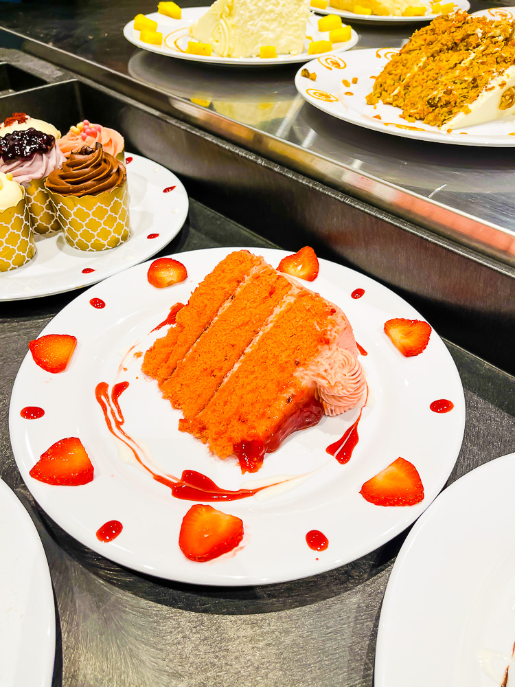 slice of three layer strawberry cake on plate with strawberry sauce and sliced strawberries.