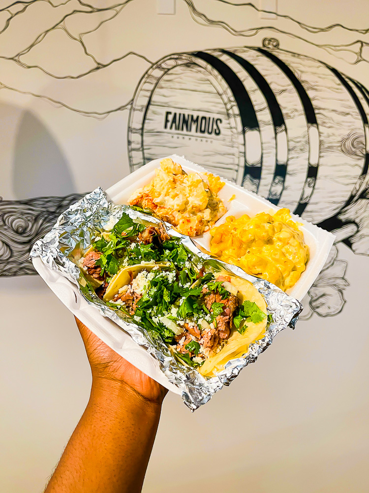 holding tray of mac and cheese, potato salad, and BBQ street tacos from Fainmous barbecue.
