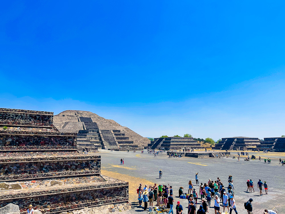 Mexico's Teotihuacan pyramid of the Moon surrounded by tourists walking around and taking pictures on a sunny day.