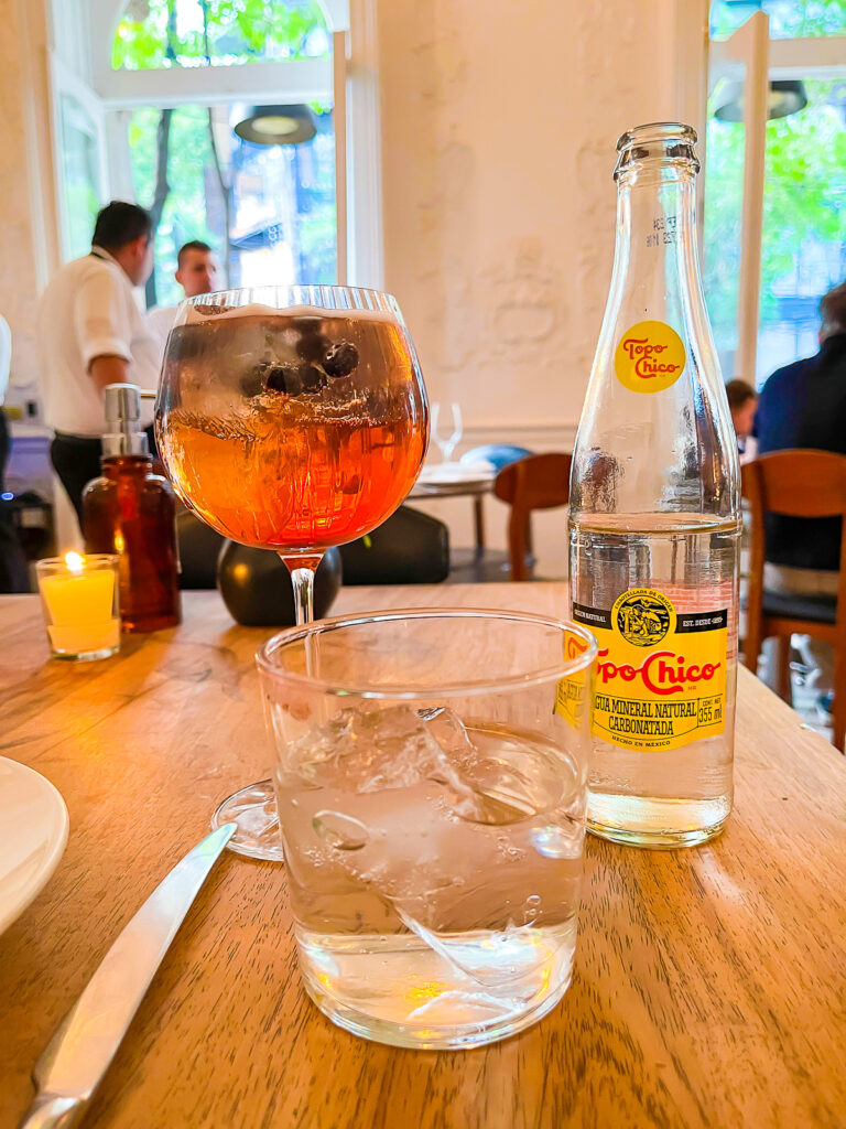 Jardí de Grosellas spritz cocktail and bottle of Top Chico on dinner table at Blanco Colima Mexico City restaurant.