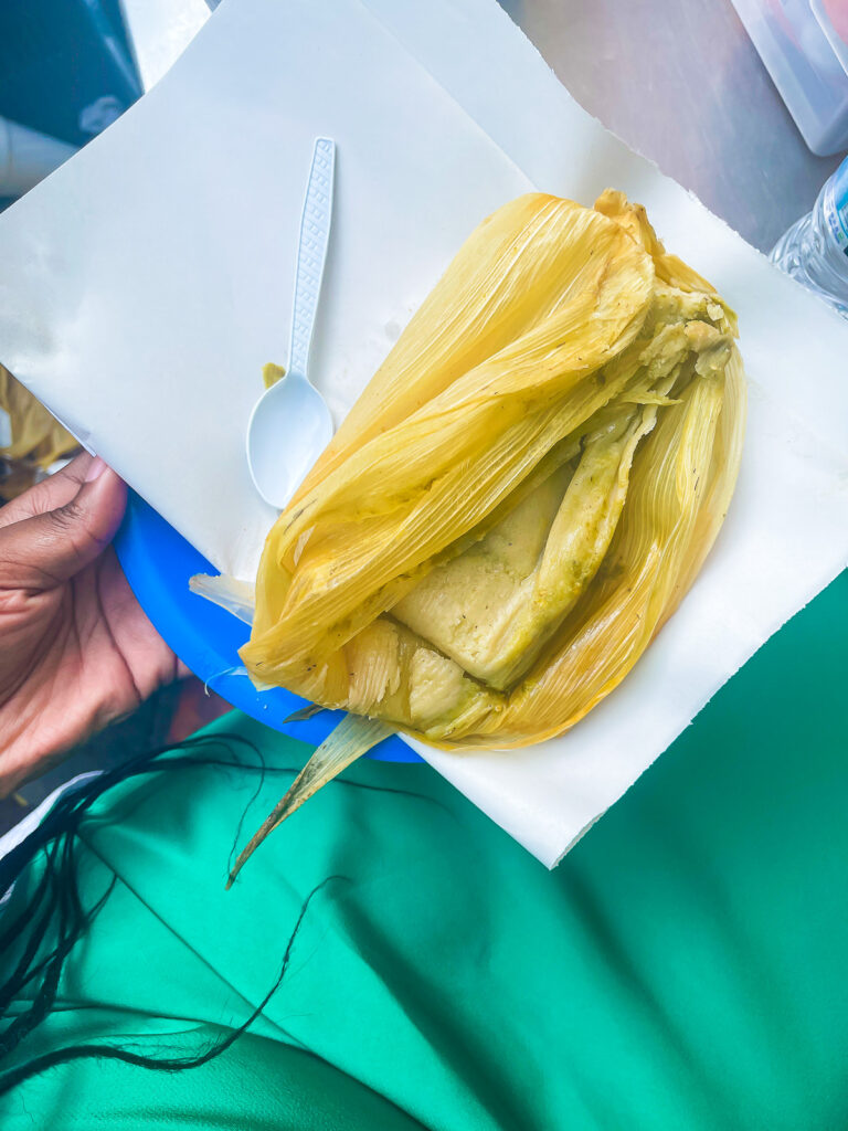 freshly made tamal verde on plate with paper napkin and plastic spoon.
