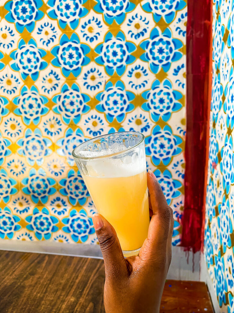 holding glass of guava pulque up against a colorful tiled wall in a restaurant near El Centro, Mexico City.
