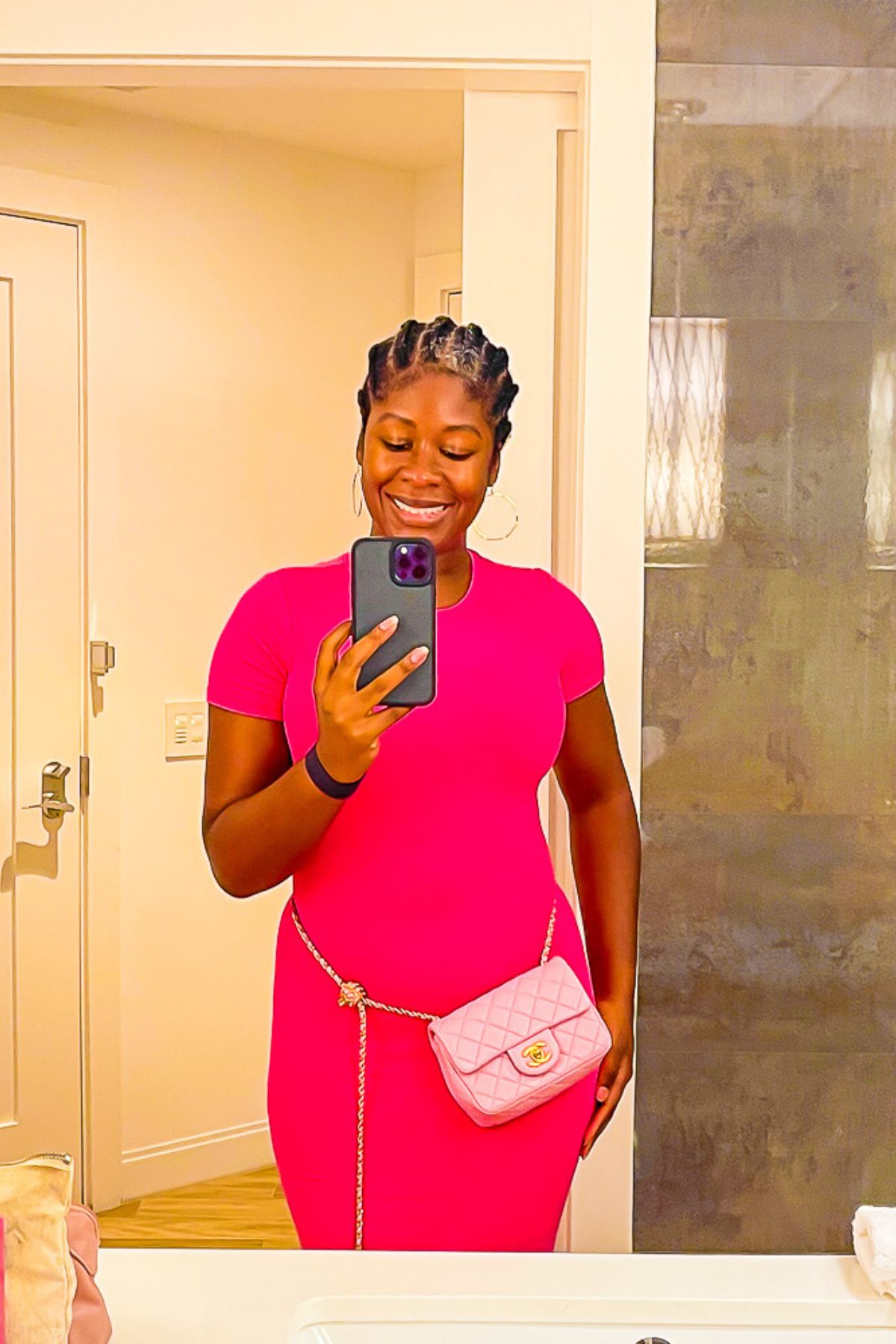 Jazzmine taking a mirror selfie in a fitted hot pink maxi dress with a pink quilted hand bag slung around her waist.