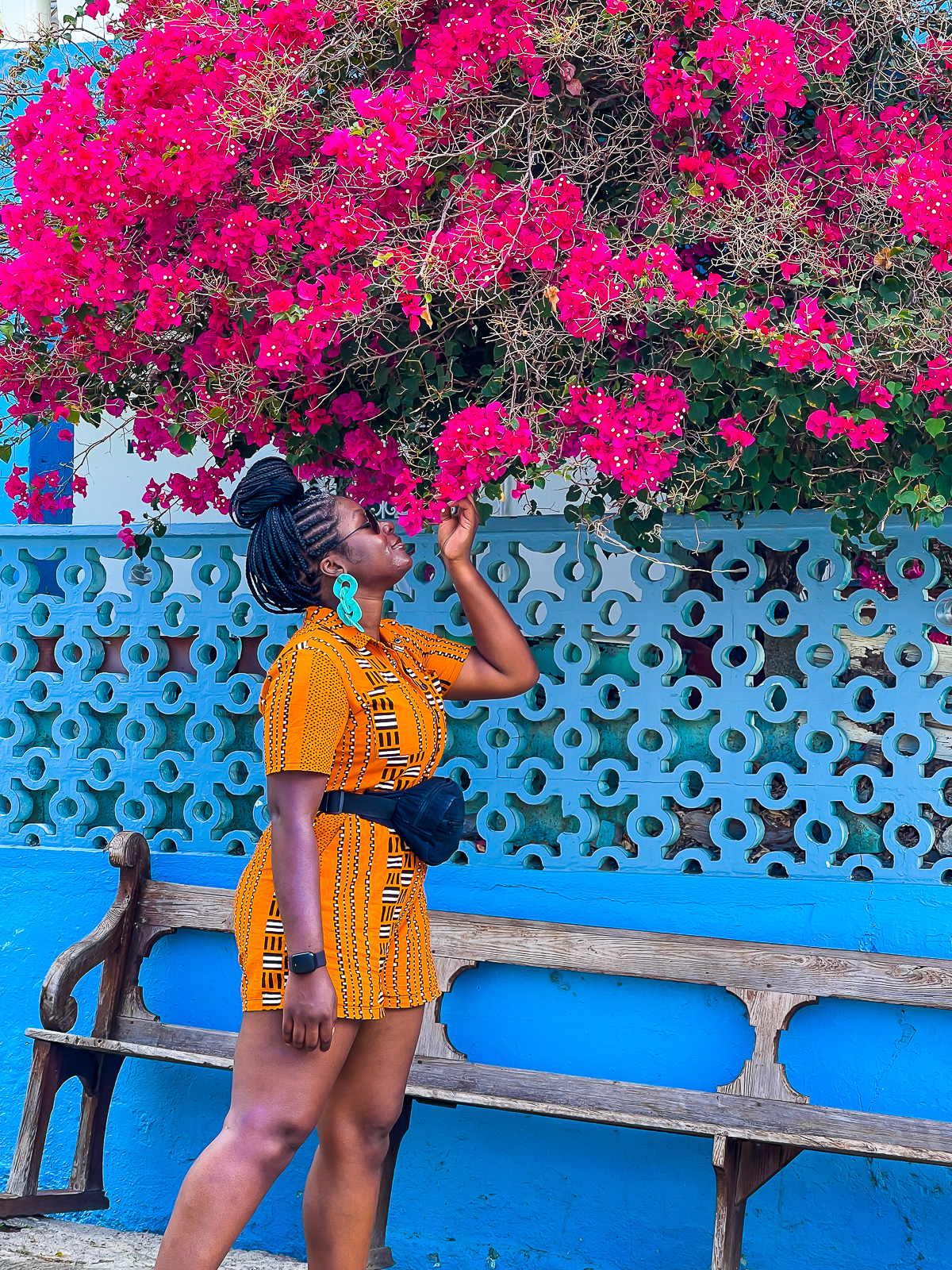 Jazzmine smelling flowers from a bougainvillea tree in Soufriere, Dominica, wearing a colorful printed romper.