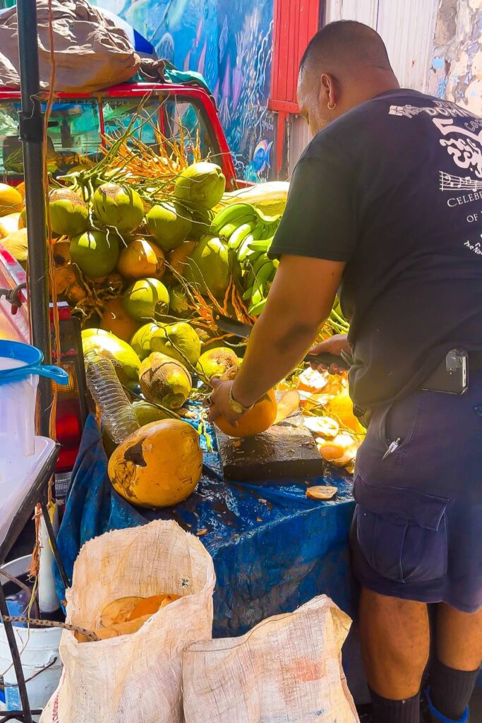 man cutting fresh Dominican coconuts at stall near Roseau Old Market.