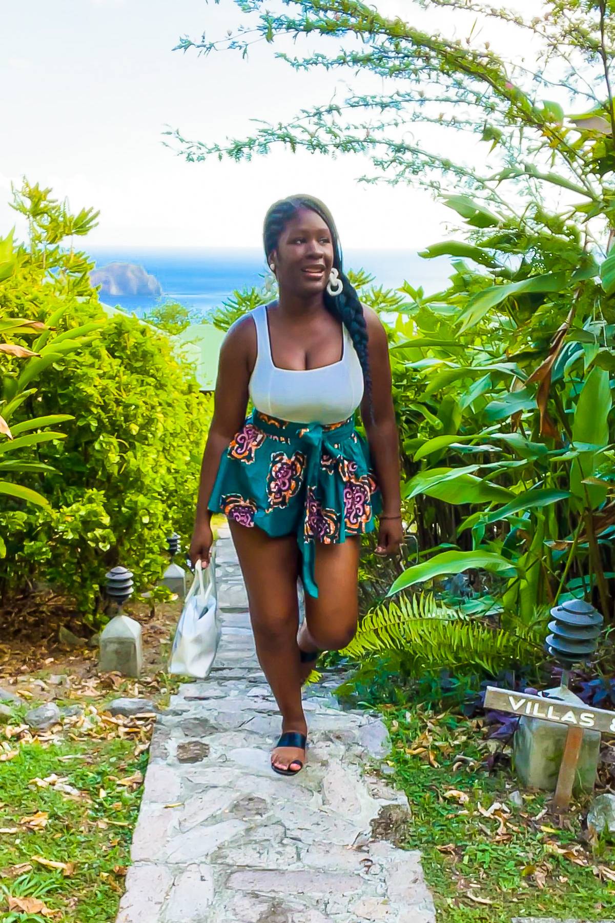 Jazzmine walking up the steps of a Dominican eco resort courtyard wearing an ankara peplum belt over cutoffs and a white tank top.