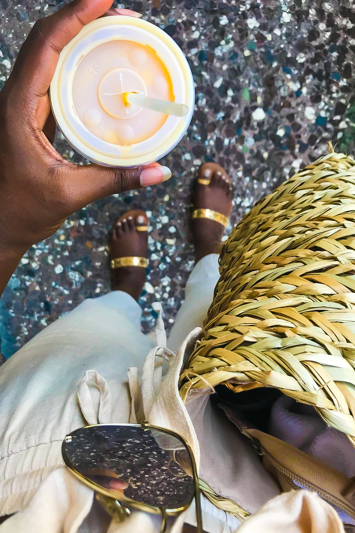 view of brown feet in gold leather sandals and hand holding a mango batida from Plaza del Mercado in Santurce.