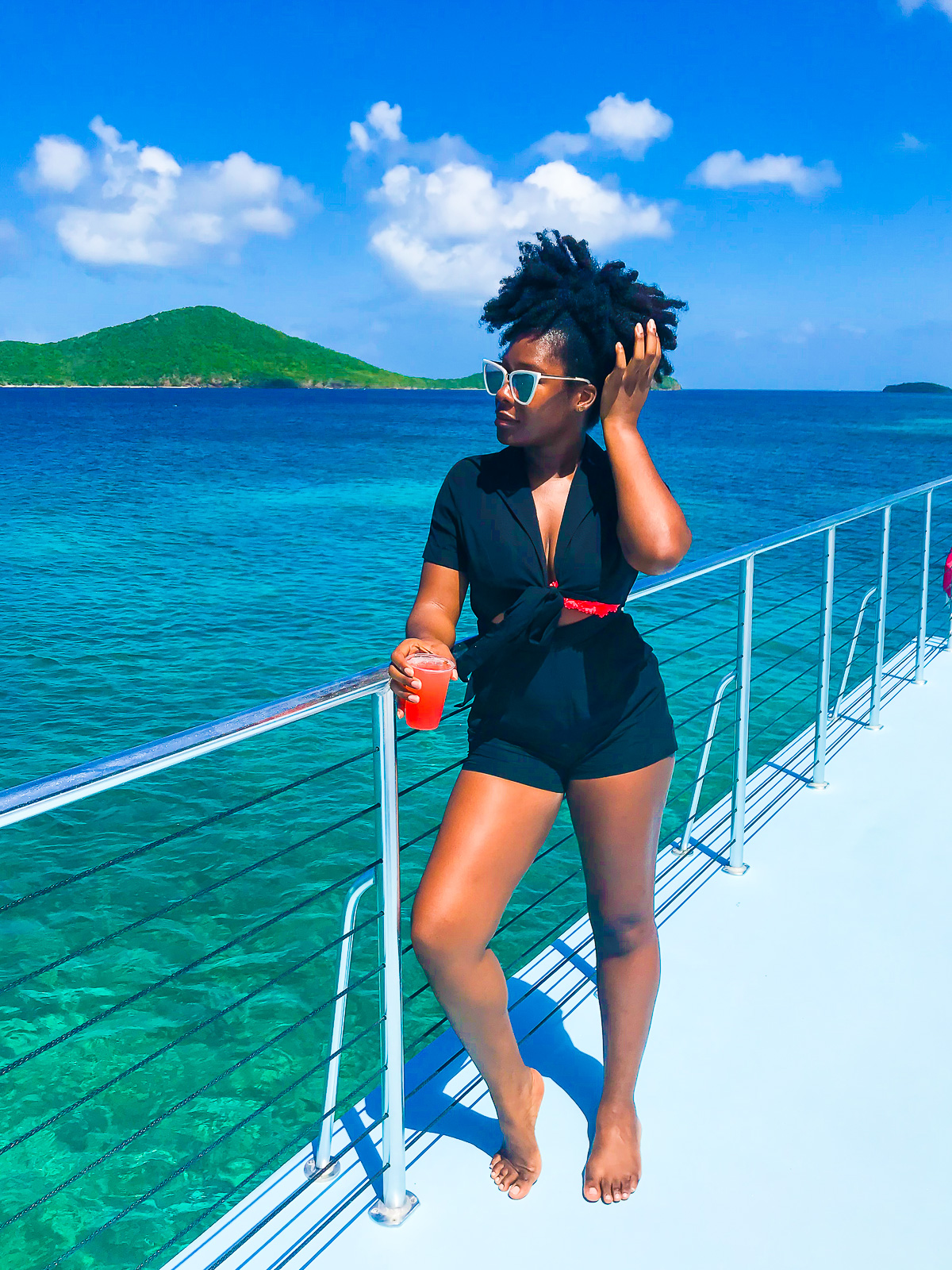 Jazzmine standing on the upper deck of a catamaran headed to Culebra, Puerto Rico, wearing a black collared romper with white cat-eye sunglasses.