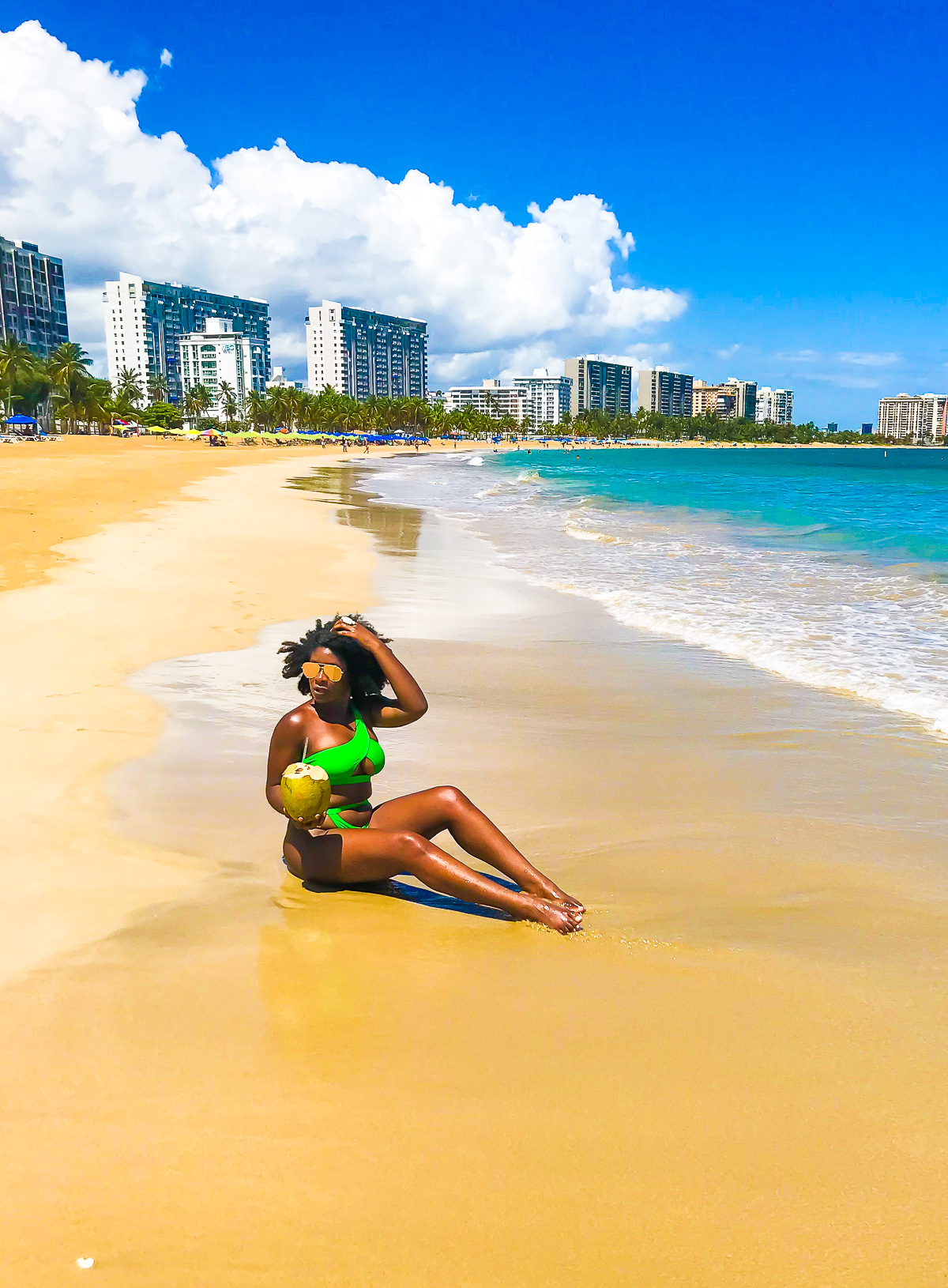 Jazzmine sitting in the sand on Isla Verde Beach on day three of a Puerto Rico itinerary 5 days long.