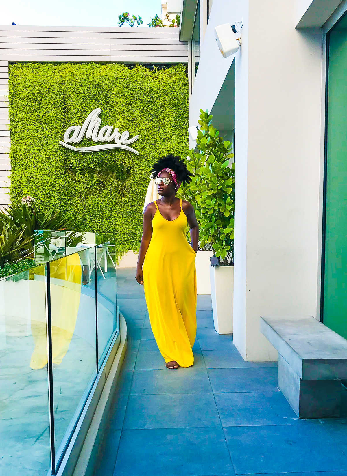 Jazzmine walking at Serafina Beach Resort wearing a flowing yellow maxi dress and polarized aviator sunglasses.