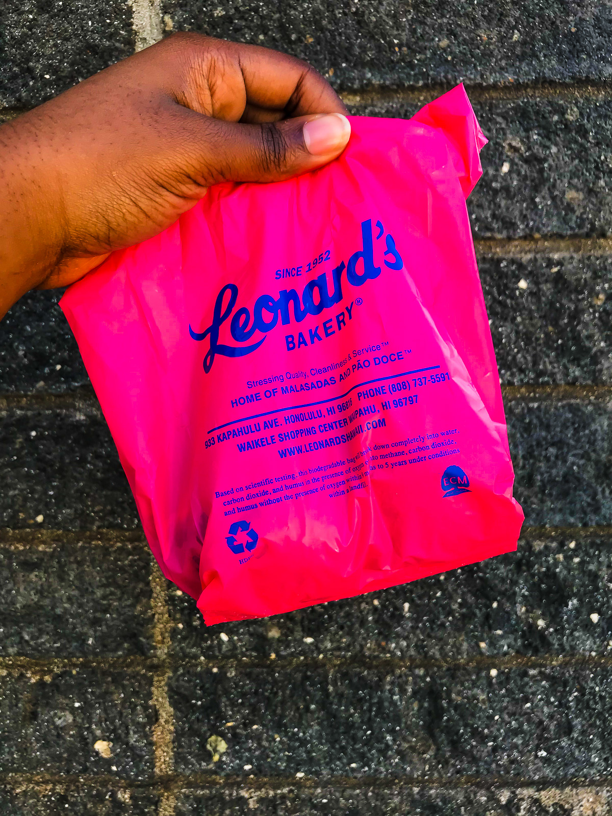 brown hand holding hot pink plastic bag from Leonard's Bakery.