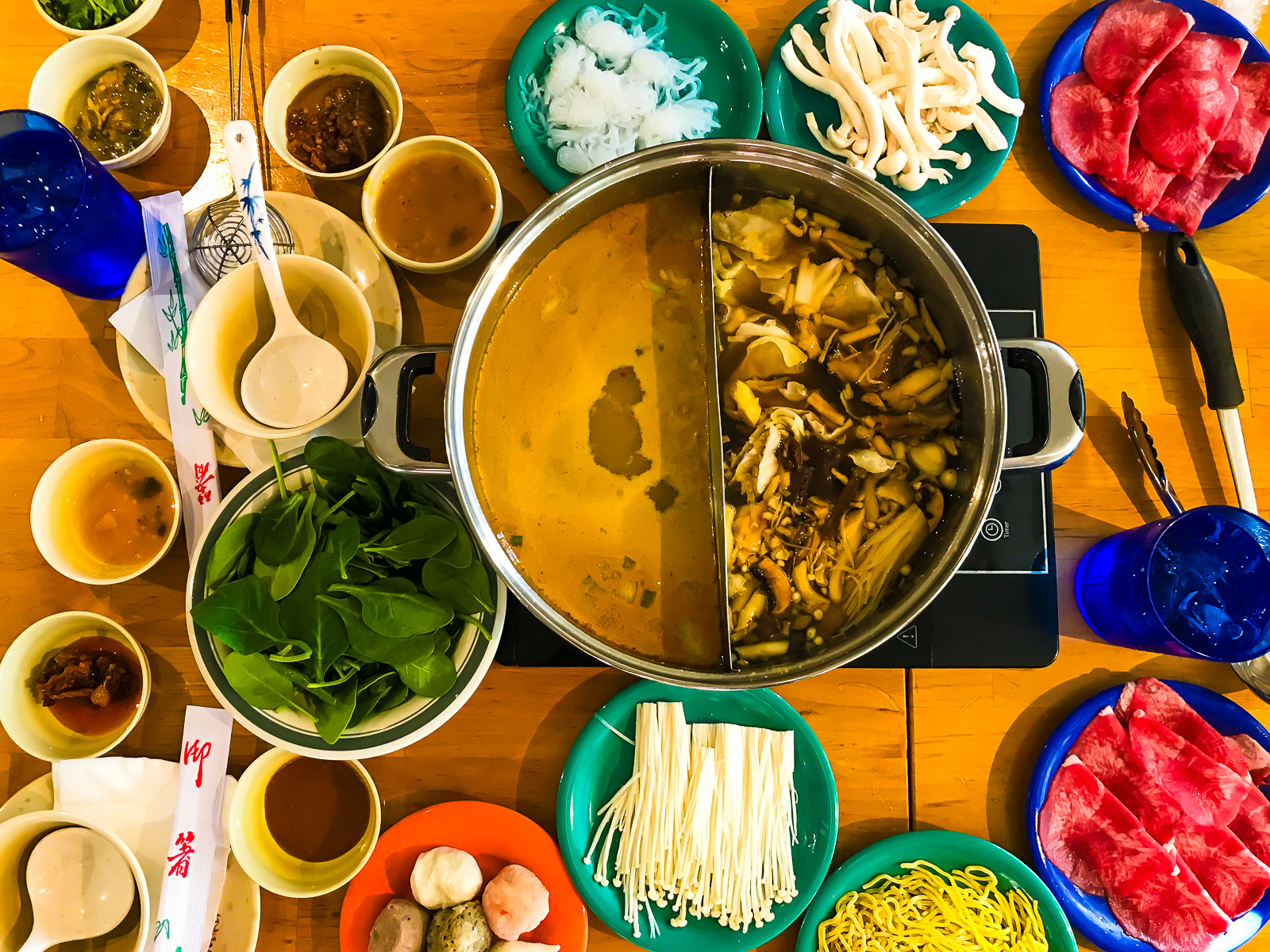 Taiwanese hot pot lunch setup with two broths fresh meats, vegetables, noodles, and seasoning at Sweet Home Cafe Waikiki, Oahu.