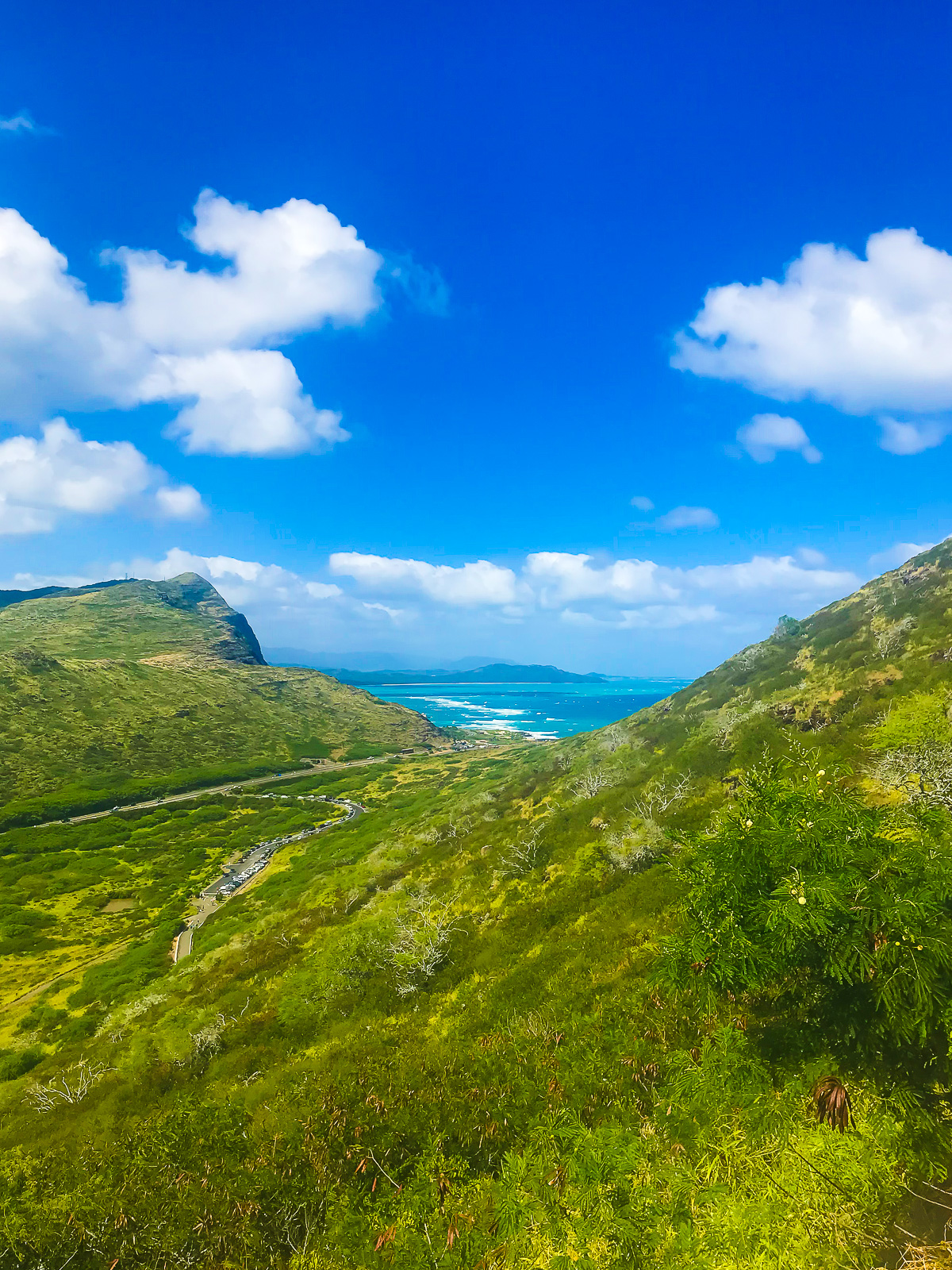 vista of blue ocean waves between two lush, grassy mountains on Oahu, Hawaii from the Makapu'u Point Trail.