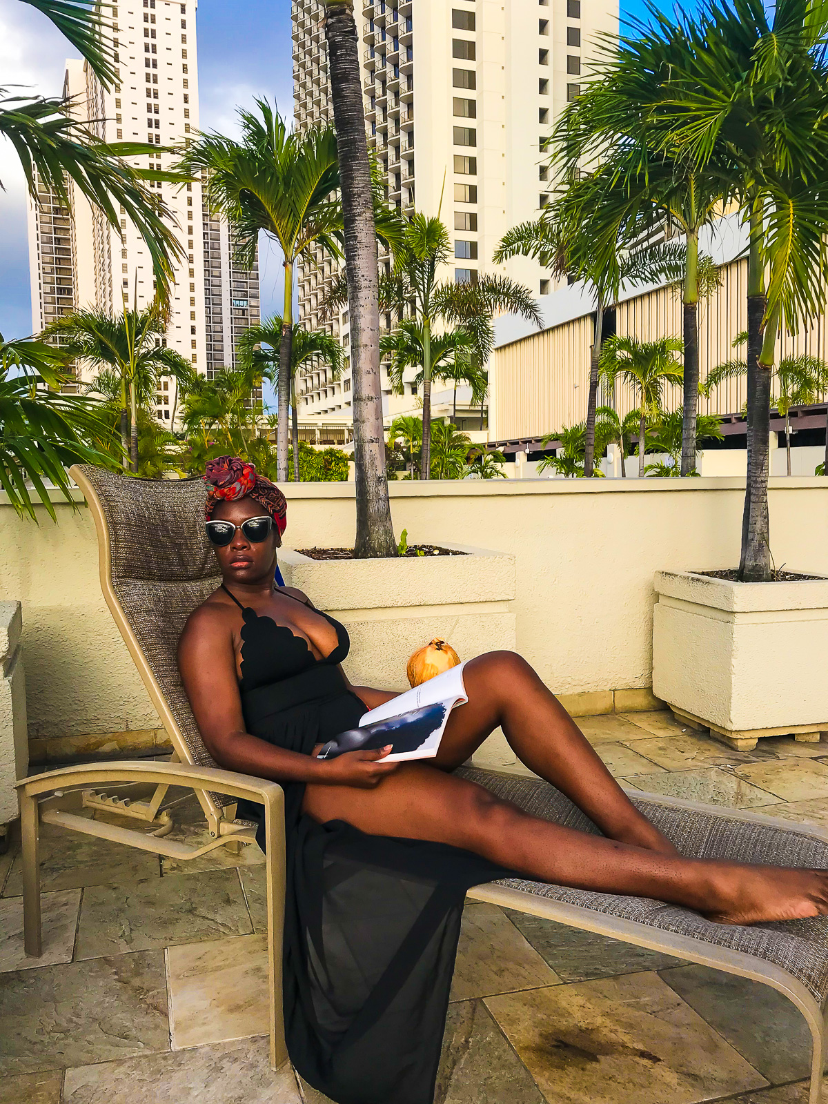 Jazzmine lounging poolside in Waikiki, Oahu, wearing a black scalloped bathing suit and red turban.