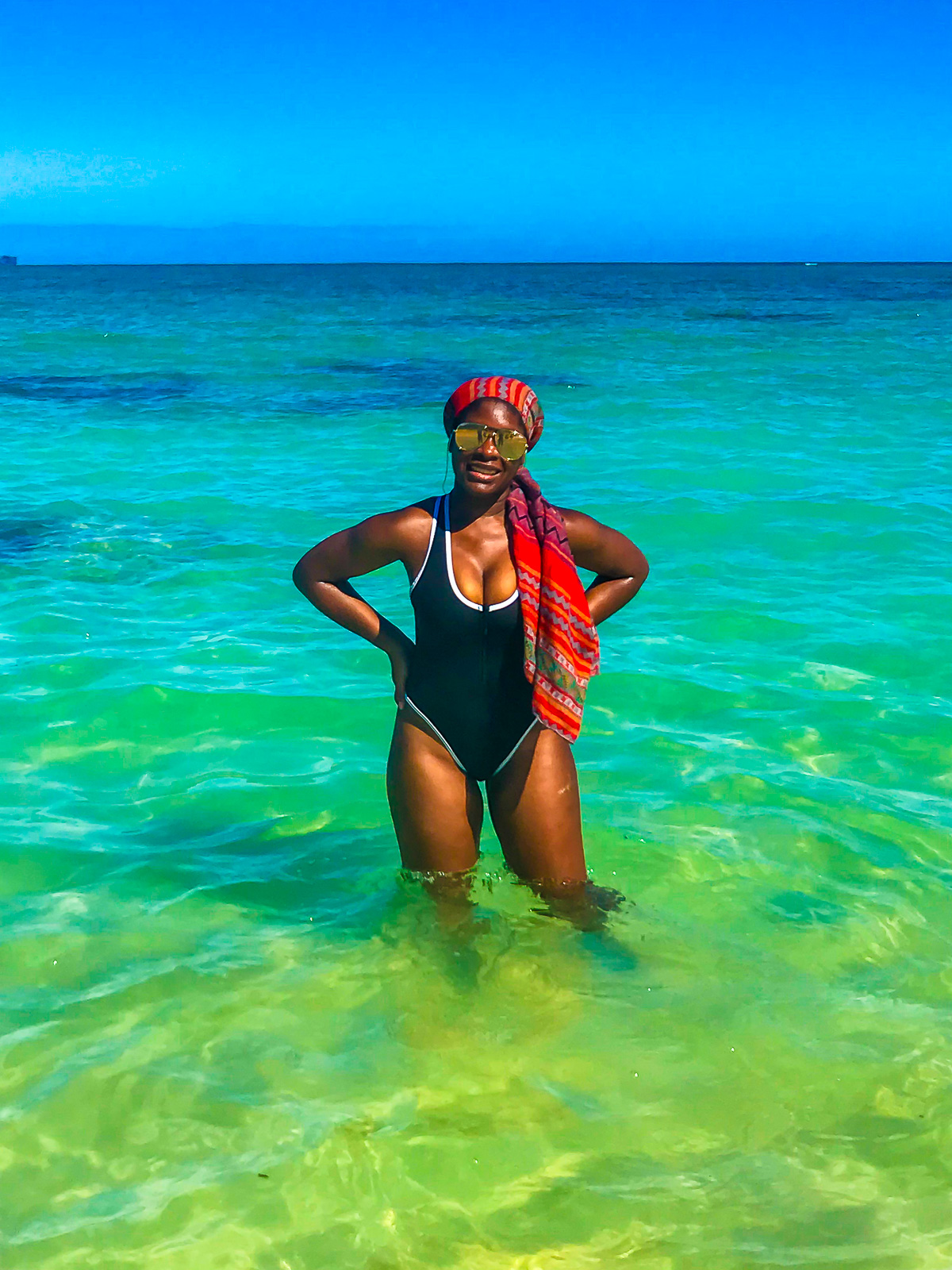 Jazzmine standing in crystal blue waters on Kailua beach wearing a black and white scuba one-piece swimsuit and long red hair scarf.