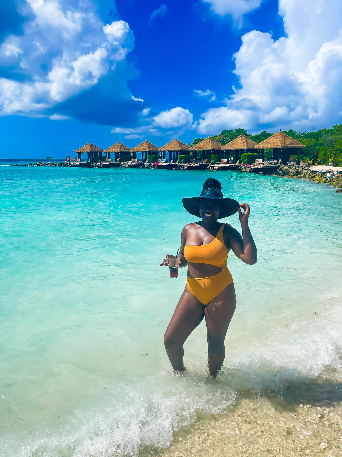 Jazzmine standing in the water off Renaissance Island in Aruba wearing a golden yellow swimsuit and black sunhat.