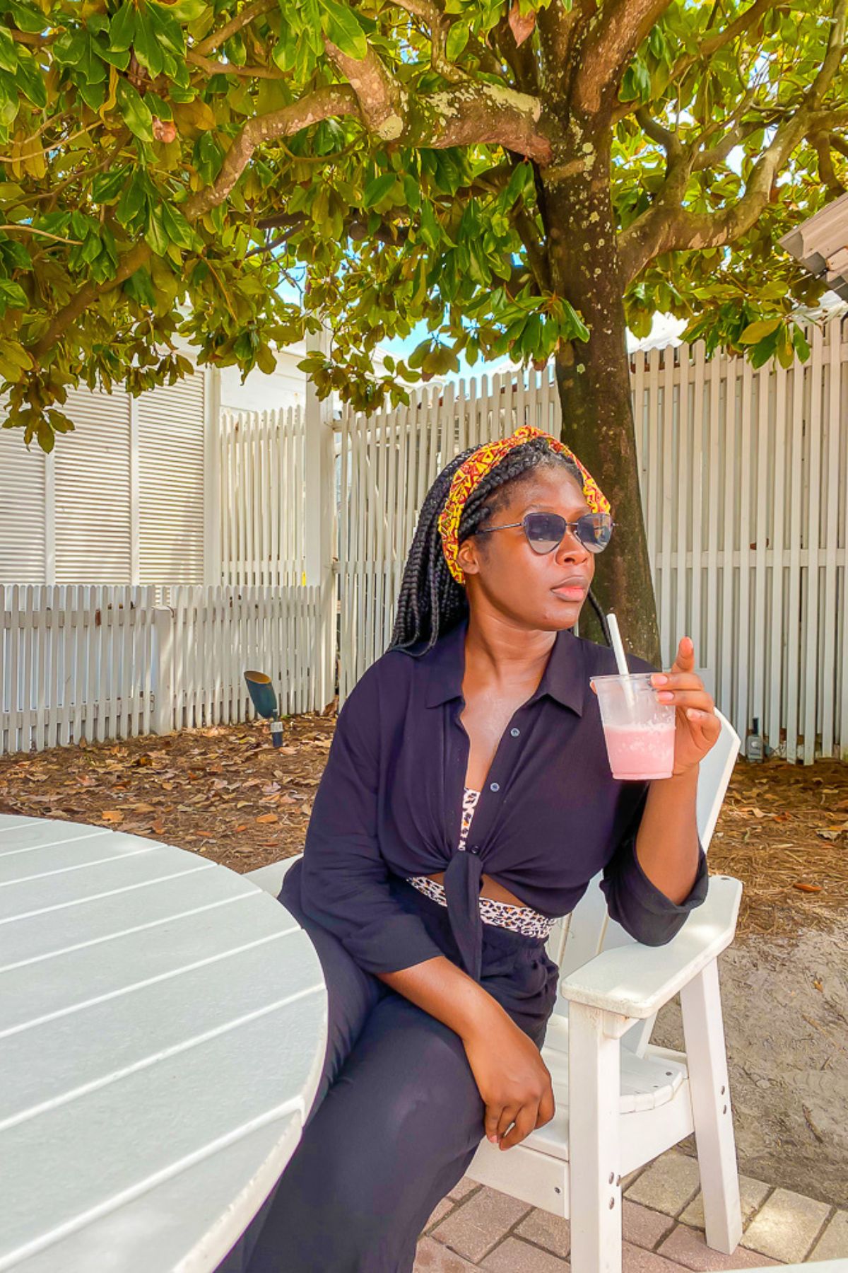 Jazzmine sitting at a beach restaurant table under the shade of a tree, drinking a strawberry smoothie.