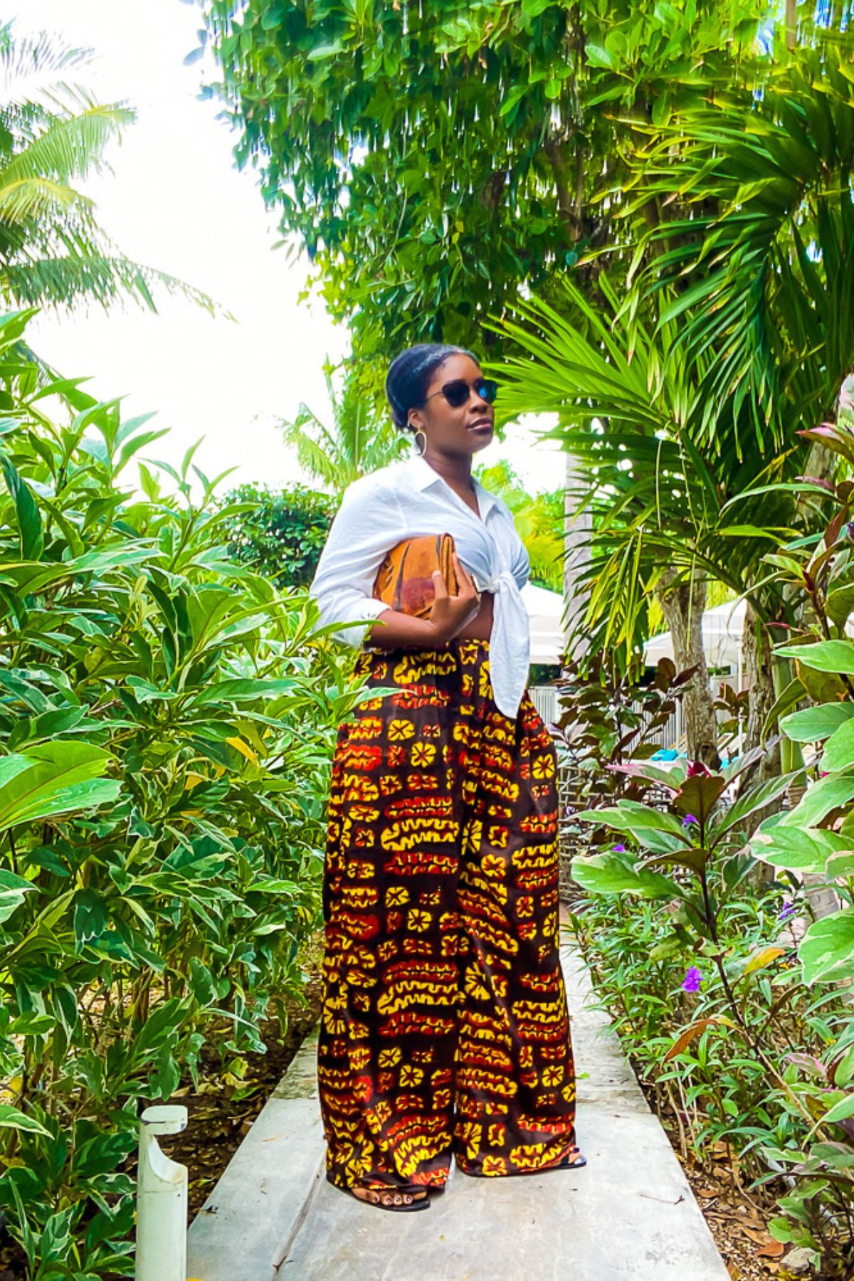 Jazzmine standing in the lush tropical courtyard of a boutique Providenciales hotel wearing printed palazzo pants and a white tie-front crop shirt.