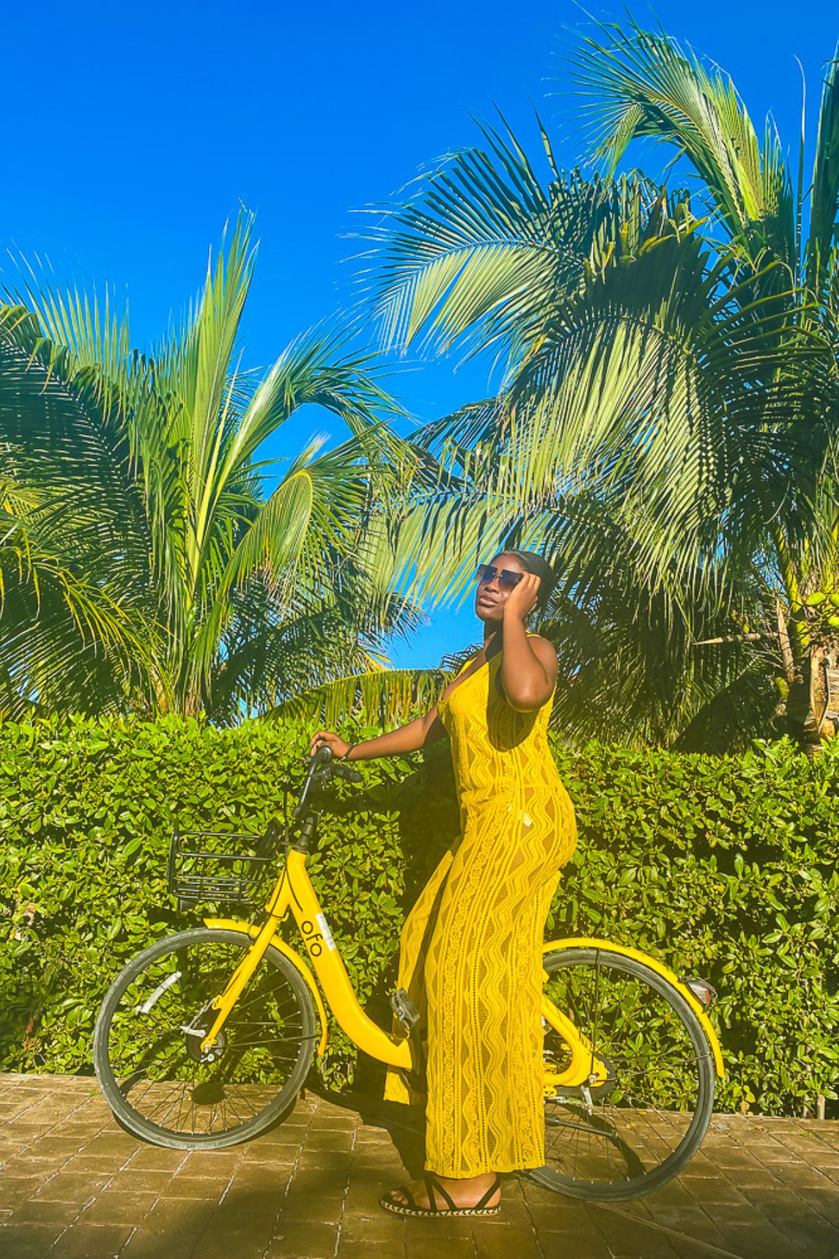 Jazzmine posing on a bright yellow bike in a matching lace jumpsuit swim cover up.
