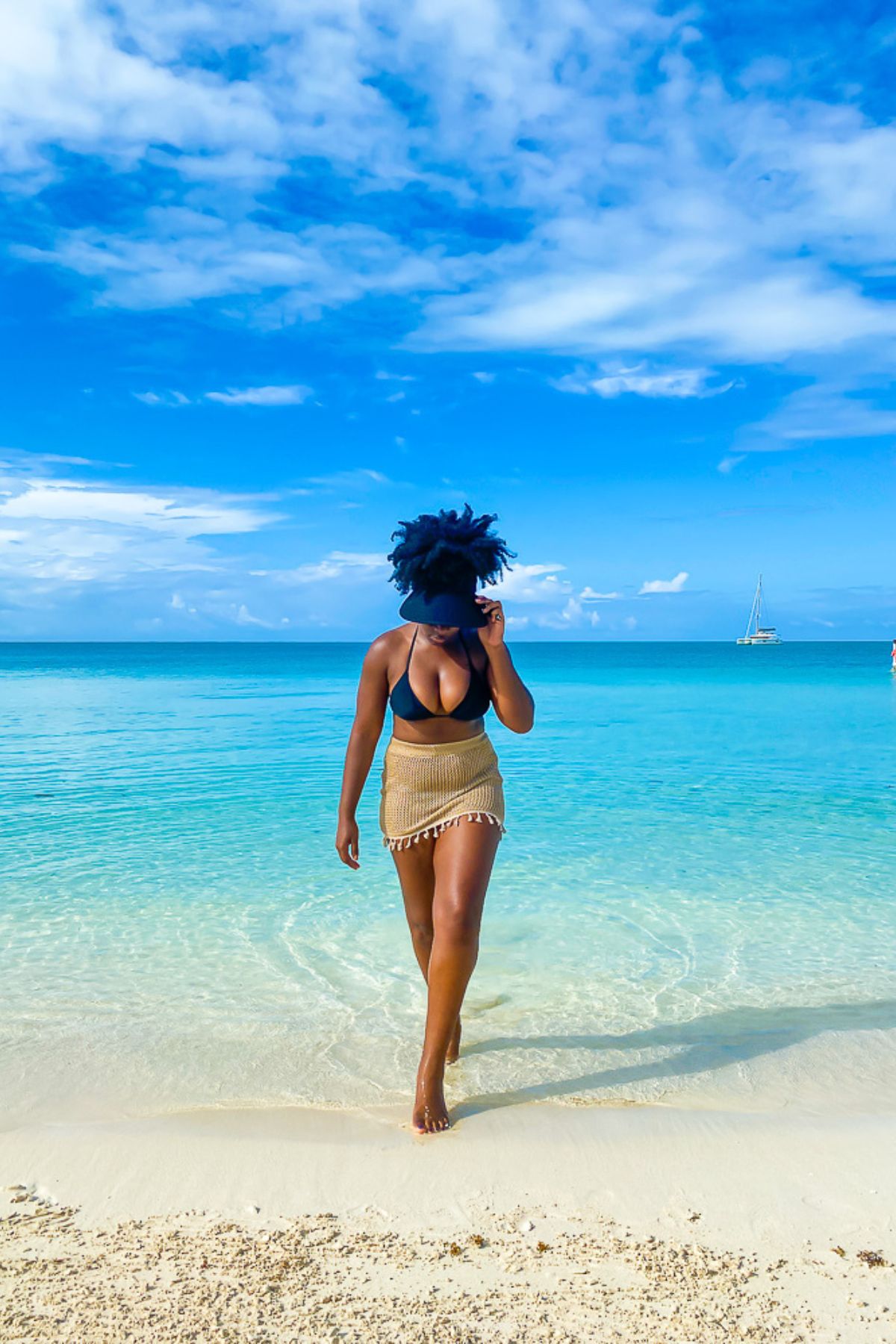 Jazzmine stepping out of the water on Sapodilla Beach wearing a black bikini with a brown crochet skirt.