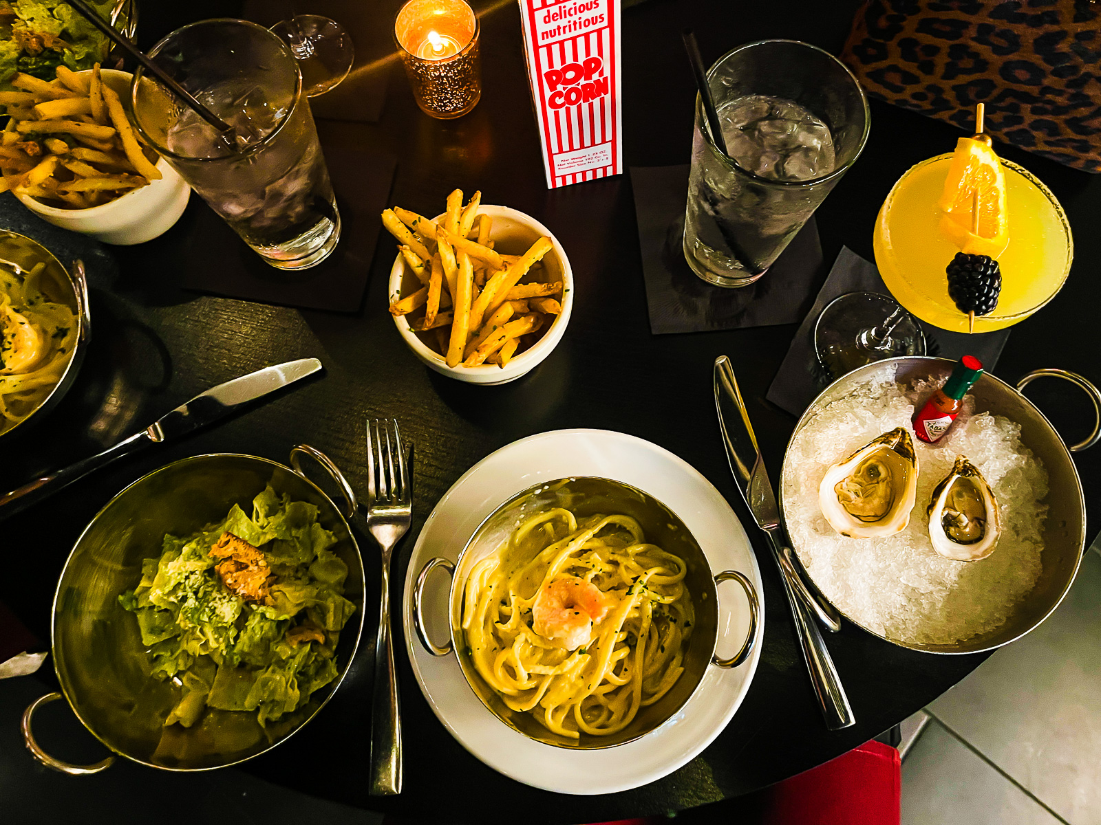 girl dinner spread at Juliet HTX, including caesar salad, shrimp pasta, oysters, truffle fries, and a passiion fruit lemon drop martini.