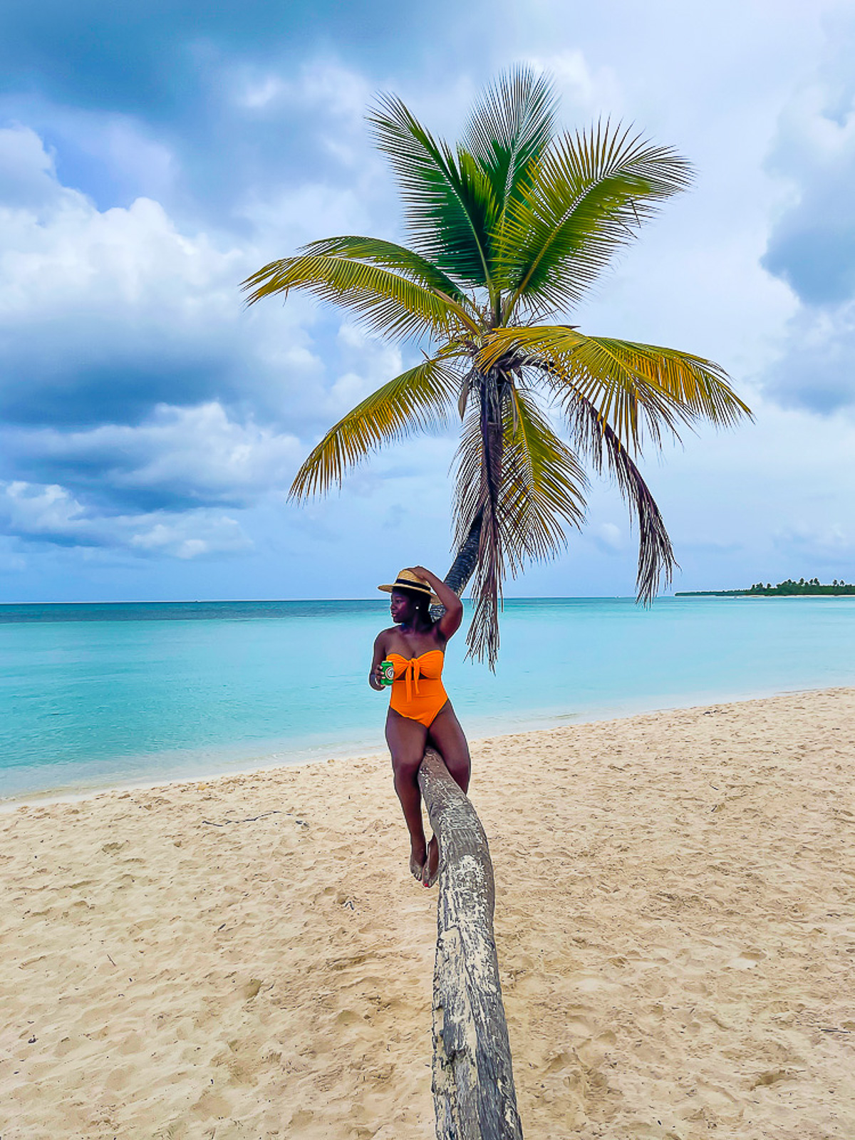 Jazzmine sitting on a curved palm tree on Playa Toro in Saona Island, holding a can of Presidente cerveza.
