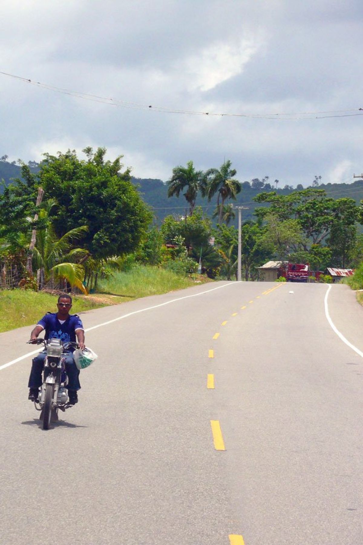 man driving a moped bike on rural road in Dominican Republic.