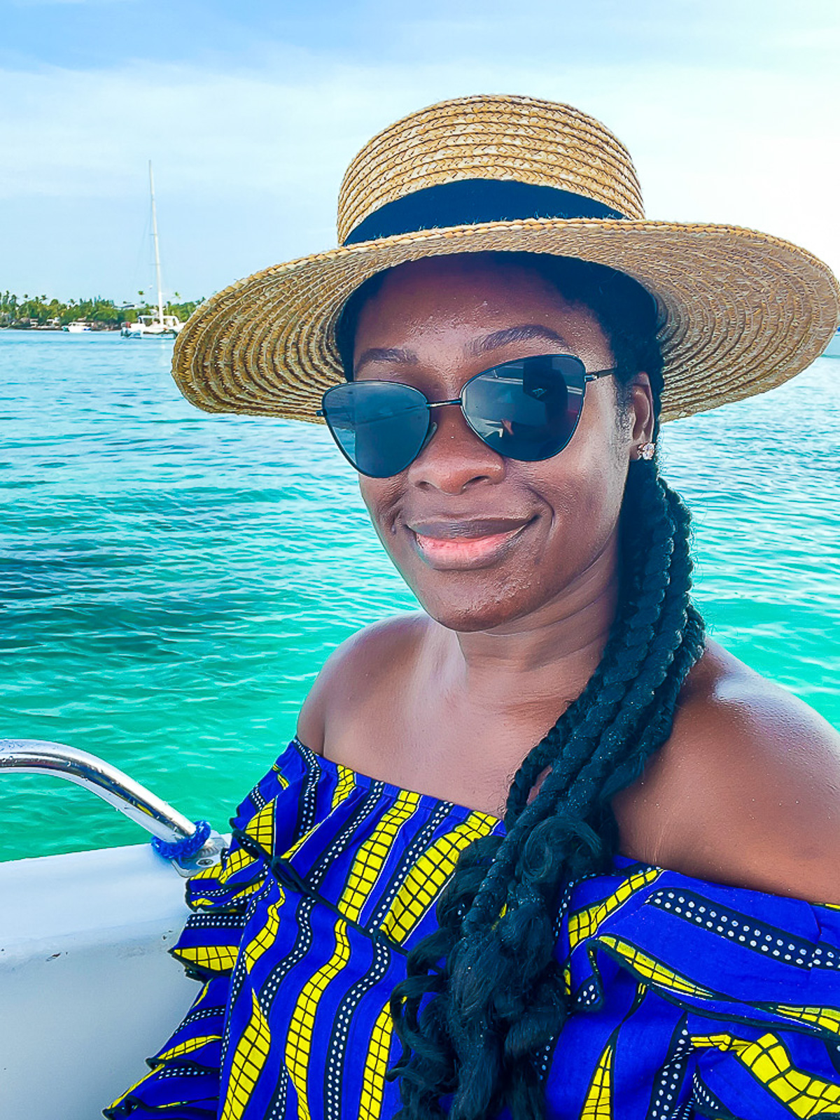 Jazzmine riding boat from Bayahibe, Dominican Republic wearing a purple and yellow off-the-shoulder top, sunglasses, and a straw sunhat.