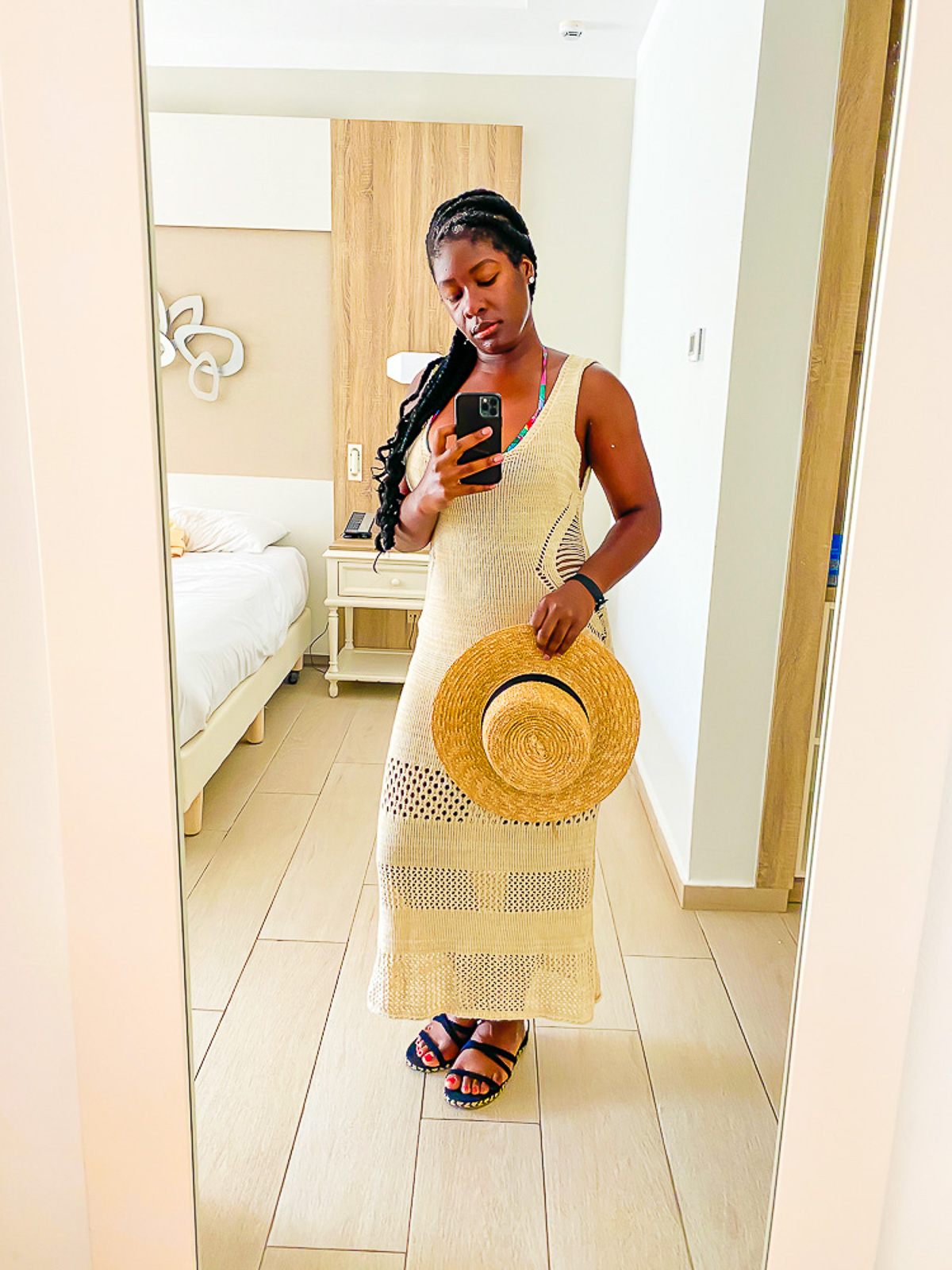 black woman taking mirror selfie at Punta Cana resort wearing a tan crochet dress and black sandals.