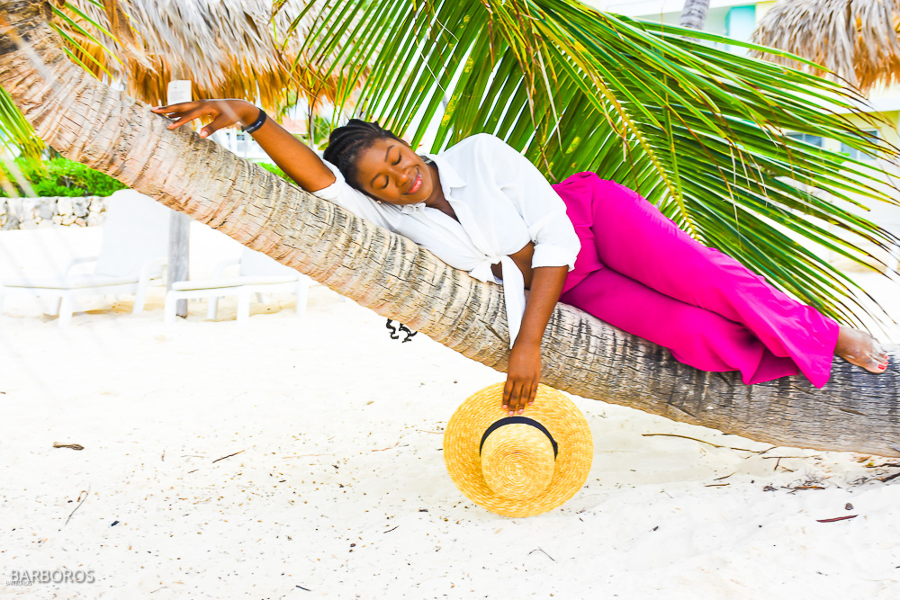 Jazzmine laying on curved palm tree in Punta Cana wearing a tie-waist crop top and fuchsia beach pants.