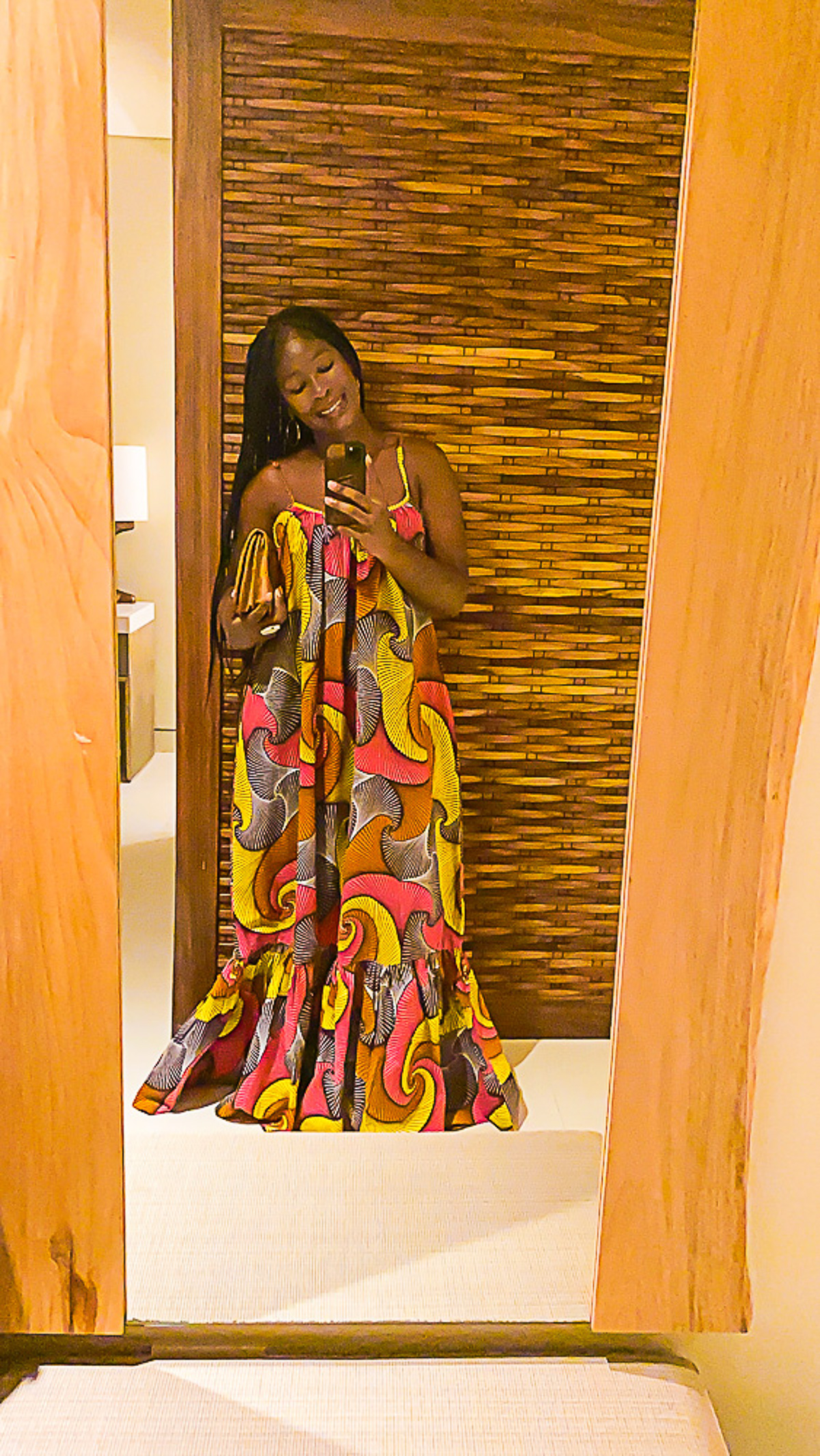 Jazzmine taking a mirror selfie in a dramatic ankara patterned maxi dress before dinner at Buccano's at Night.