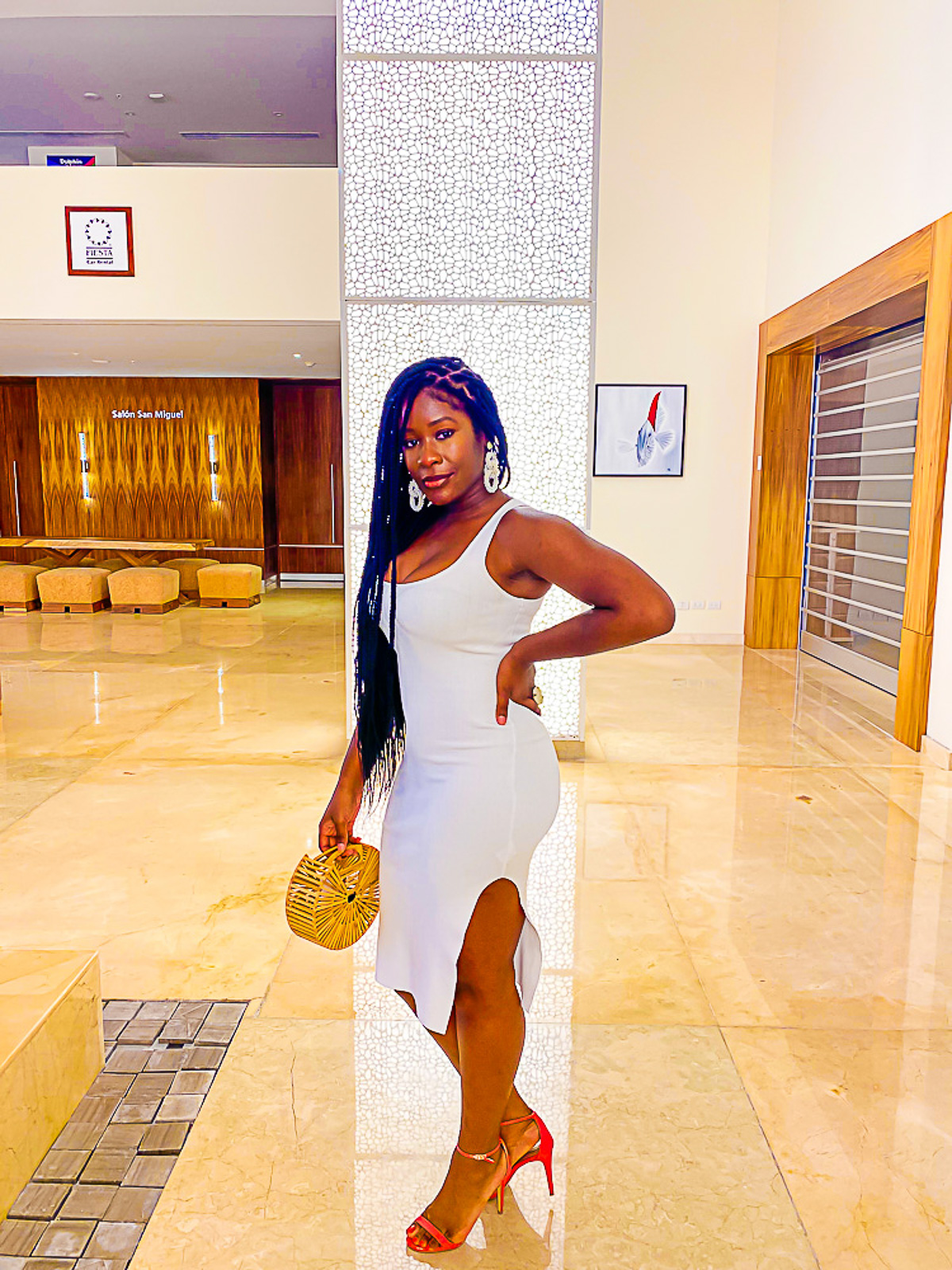 Jazzmine posing in the Westin Cozumel lobby in a white midi dress, holding a wooden handbag.