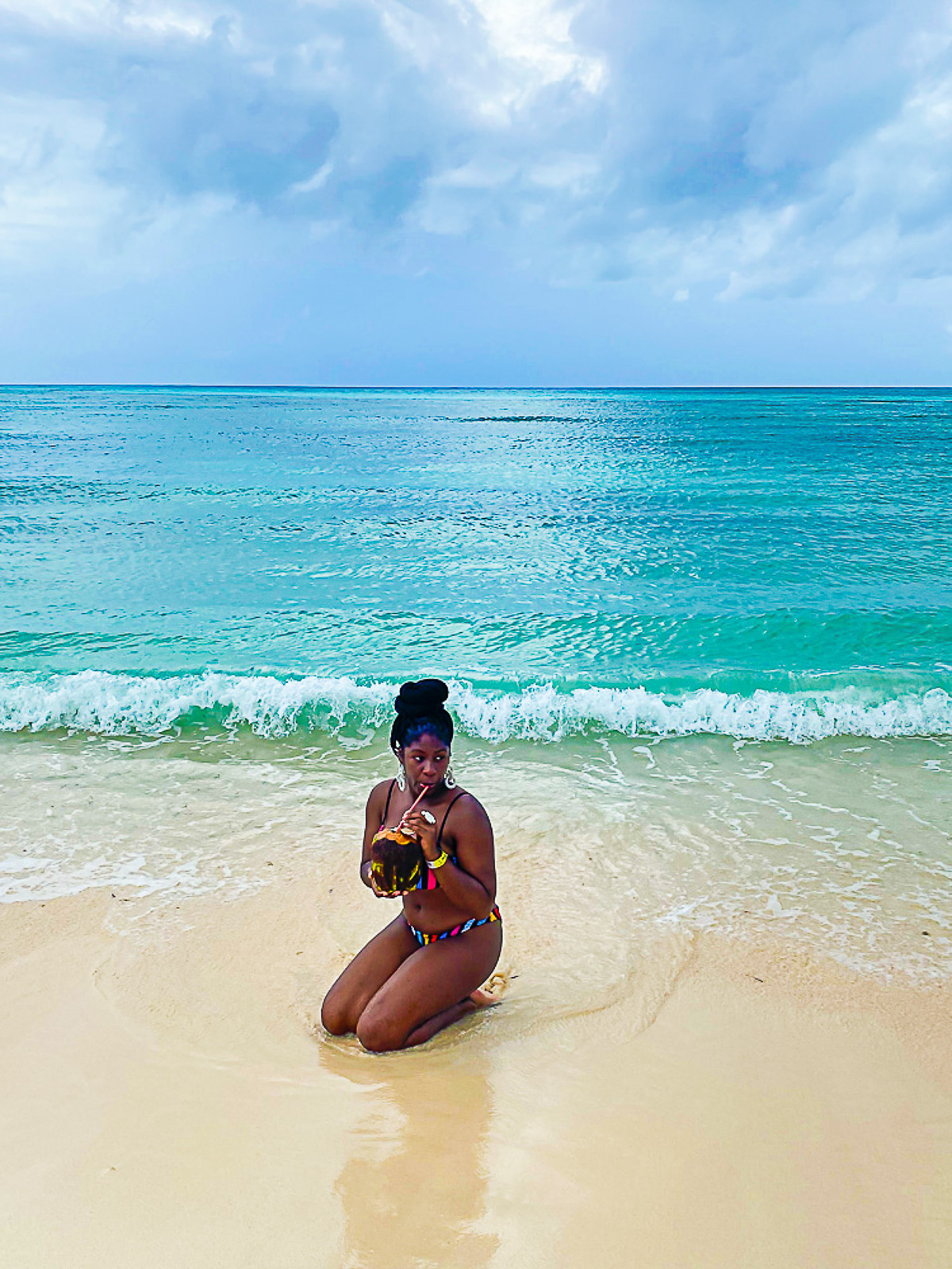 Jazzmine sitting in the sand sipping from a fresh coconut with turquoise water splashing behind her on Cozumel Island.