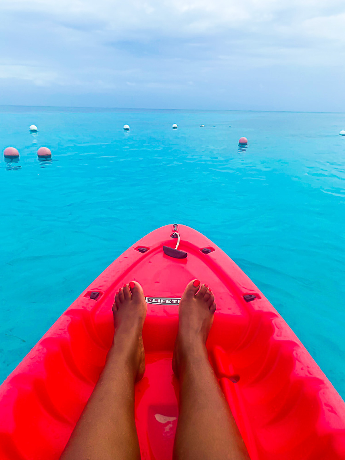 brown legs on a bright red kayak in Caribbean Sea waters off the coast of Cozumel.