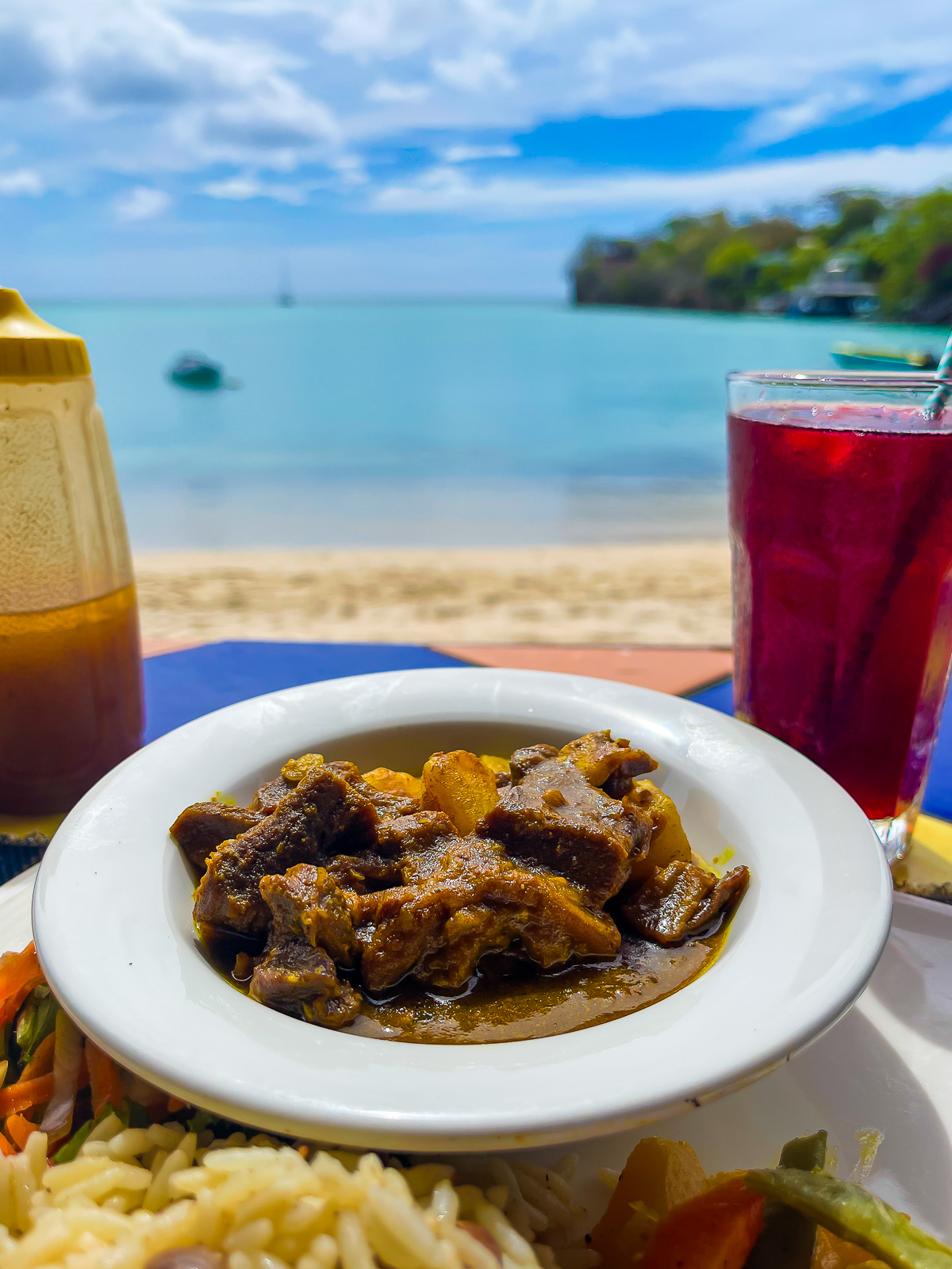 Jamaican-style curry goat, rice and peas, and sorrel served with a view at BBC Beach in Morne Rouge, Grenada.