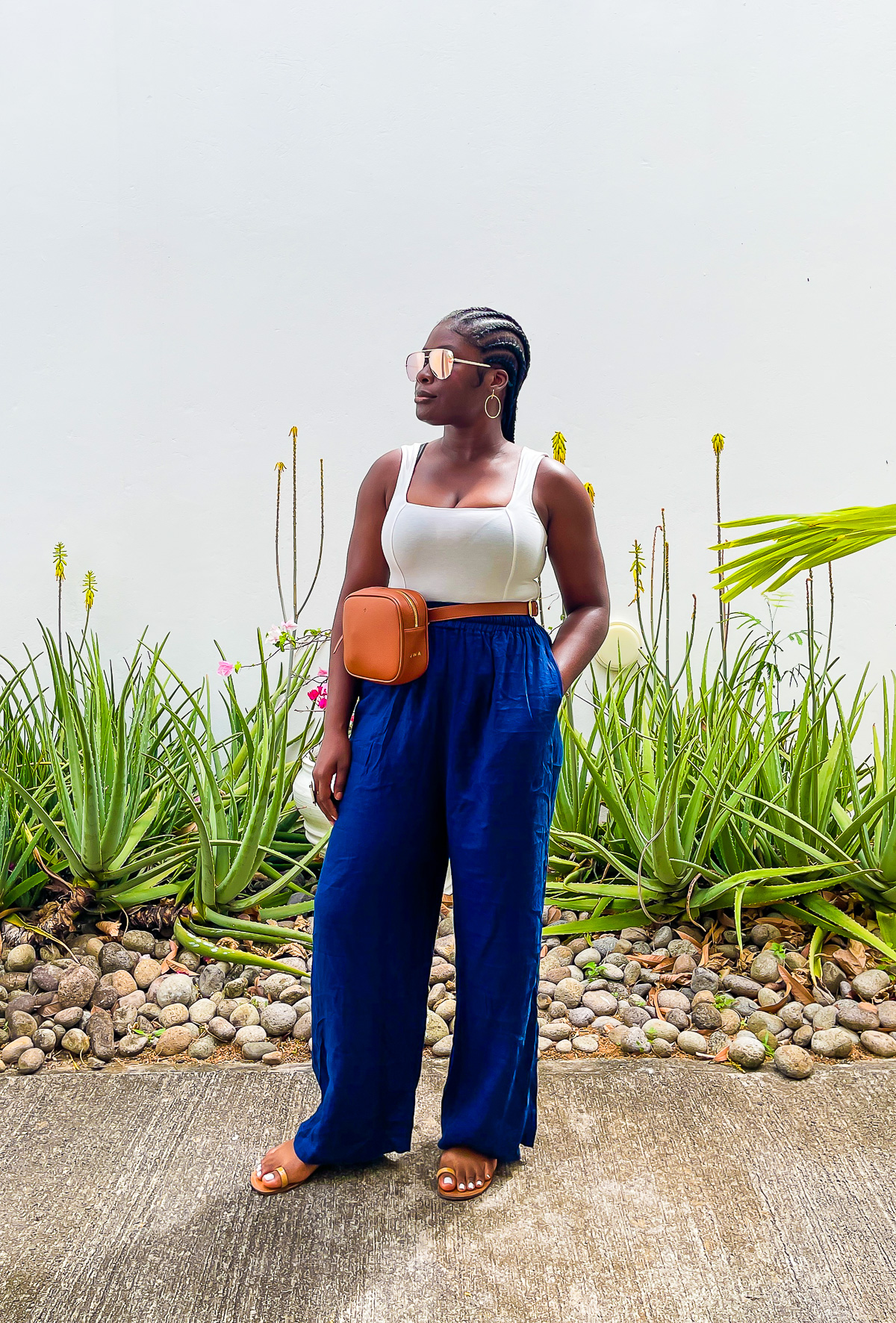 Jazzmine posing on Grenada beach resort in dark blue linen pants, a cream-colored tank top, polarized aviators, and sandals.