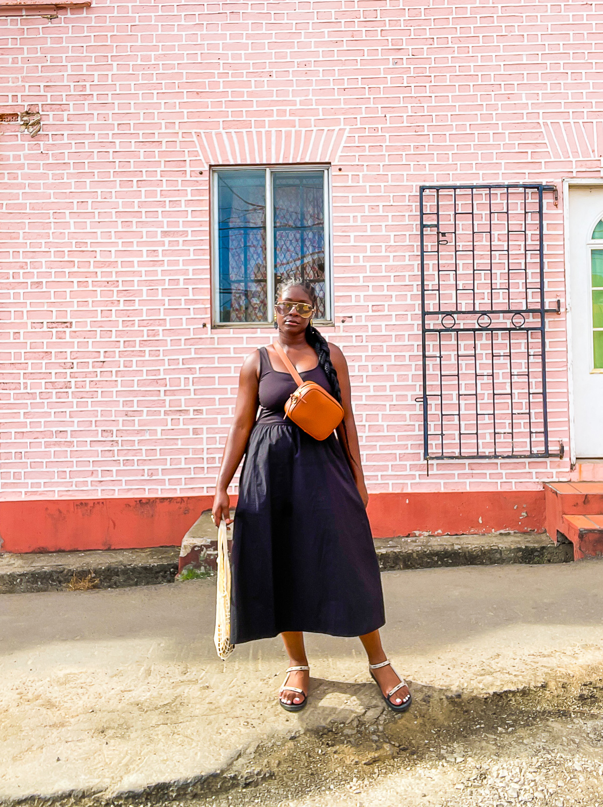 Jazzmine standing in front of a pink brick wall near St. George Market in Grenada, West Indies, wearing a black mixed media A-line dress.