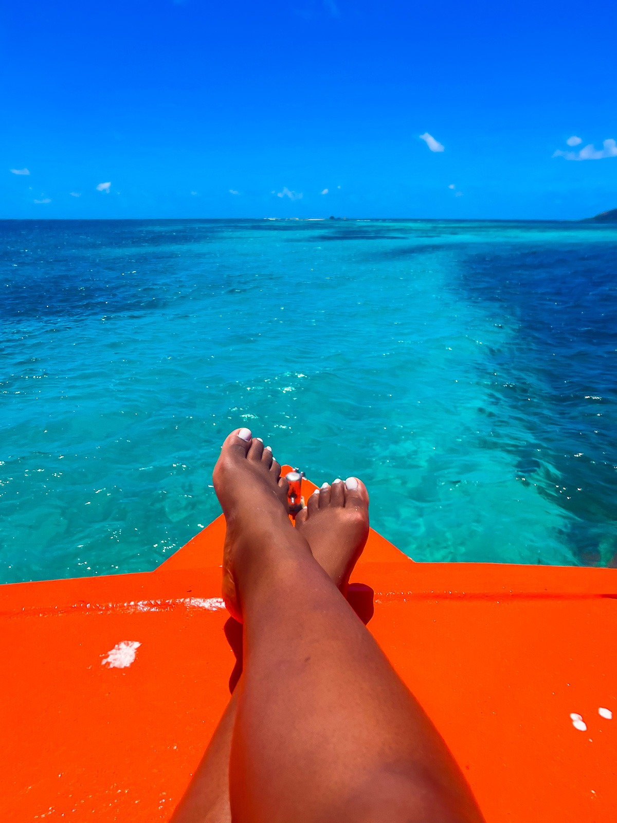 brown feet propped up on the orange deck of a speedboat sailing over crystalline Caribbean waters near the Grenadines.